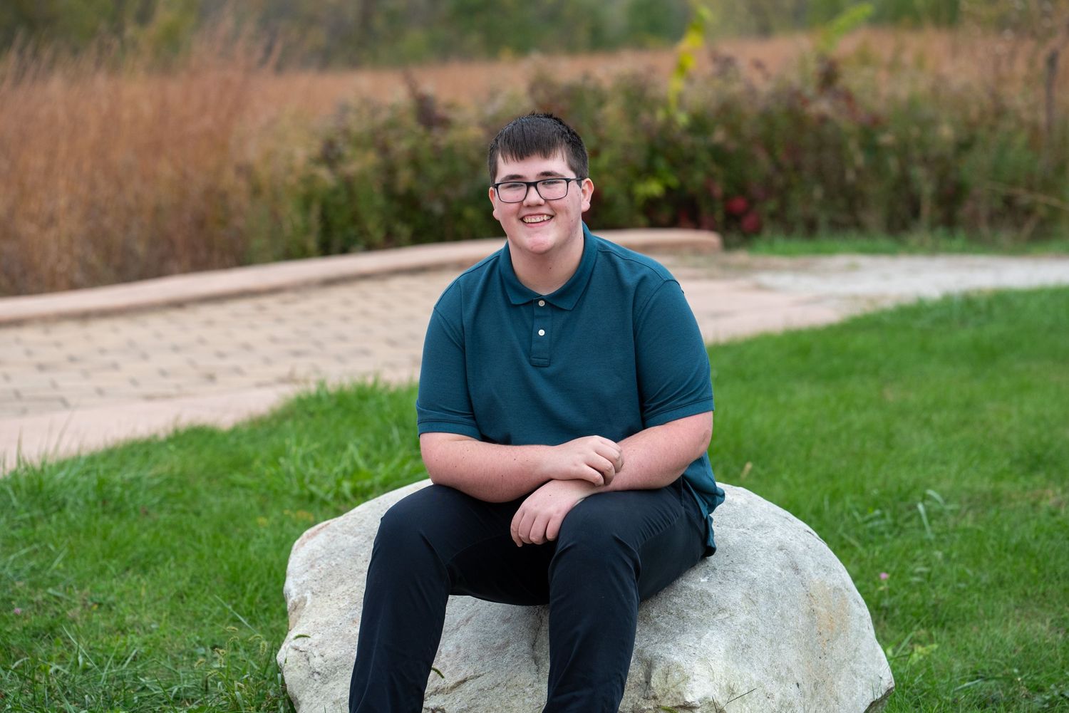 Person in dark clothing sitting casually on a large rock outdoors during a photo session.