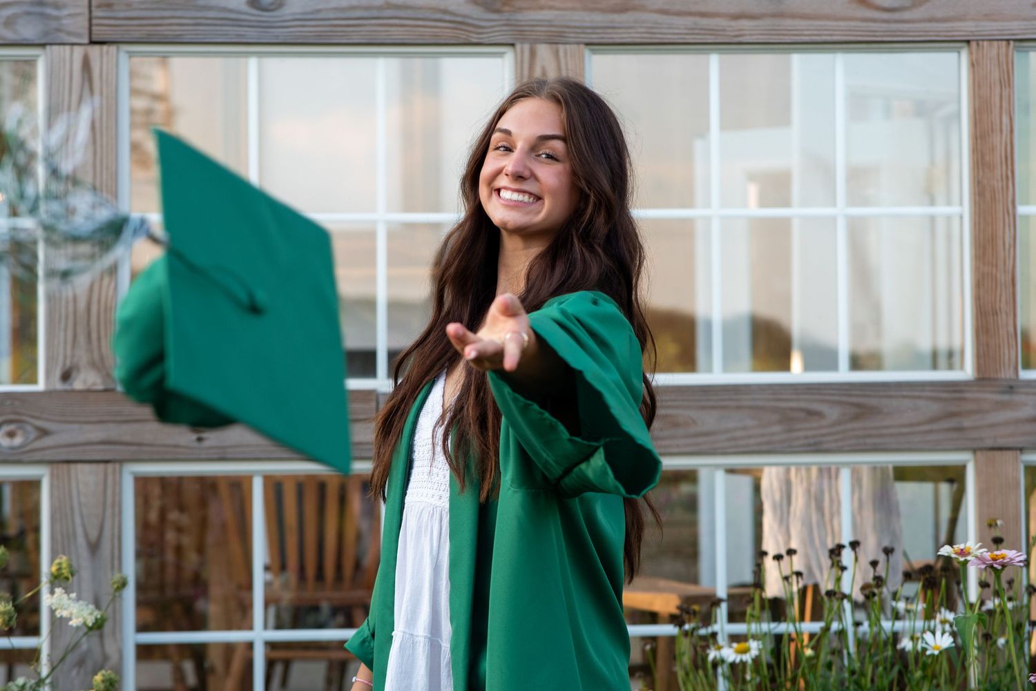 Person in green graduation gown celebrating outdoors with enthusiasm.