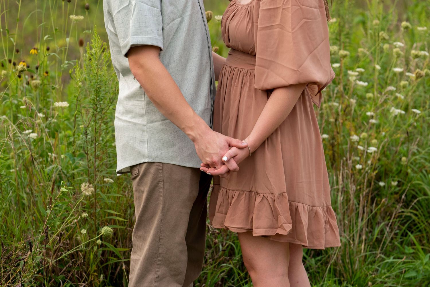 Couple holding hands in a field of wildflowers during a summer engagement photo session.