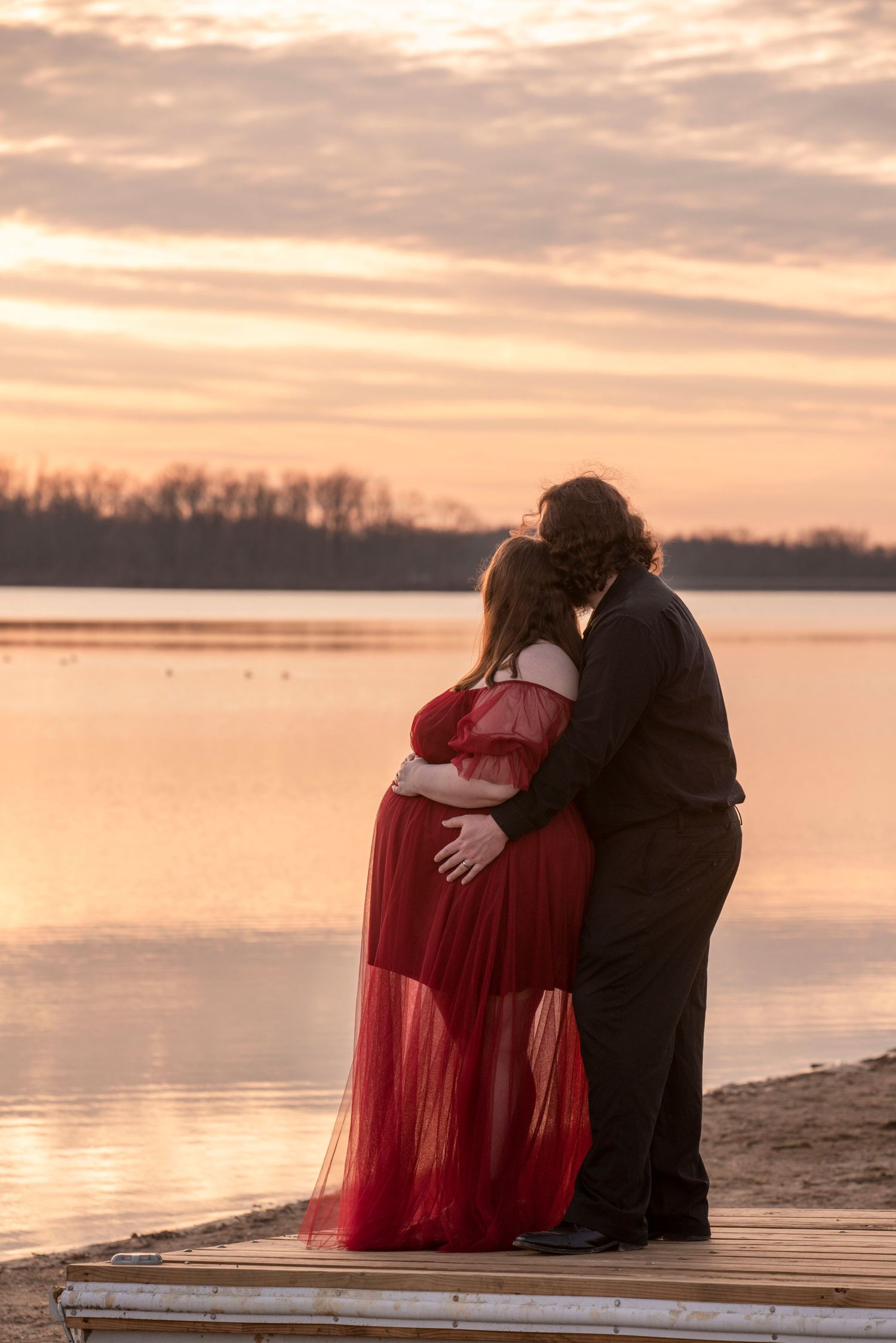Couple shares intimate moment on beach during sunset maternity session.