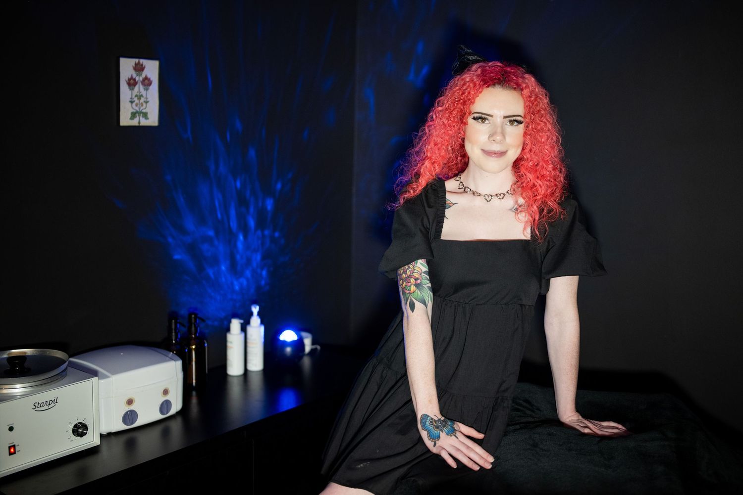 Woman with bright red hair poses dramatically against dark background with blue lighting.