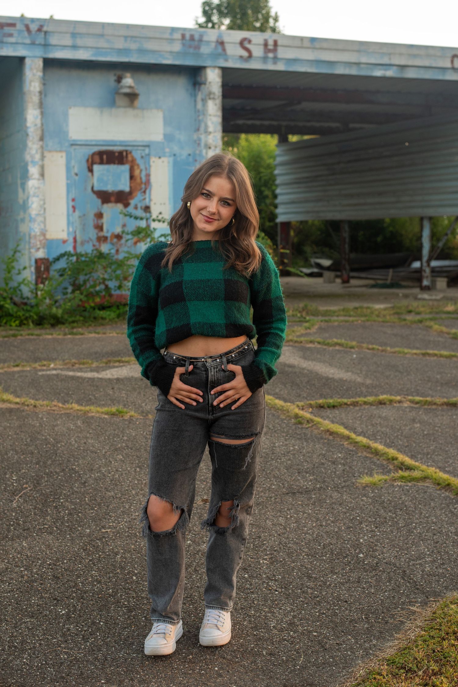 Urban fashion shoot featuring ripped jeans and green sweater against industrial backdrop.