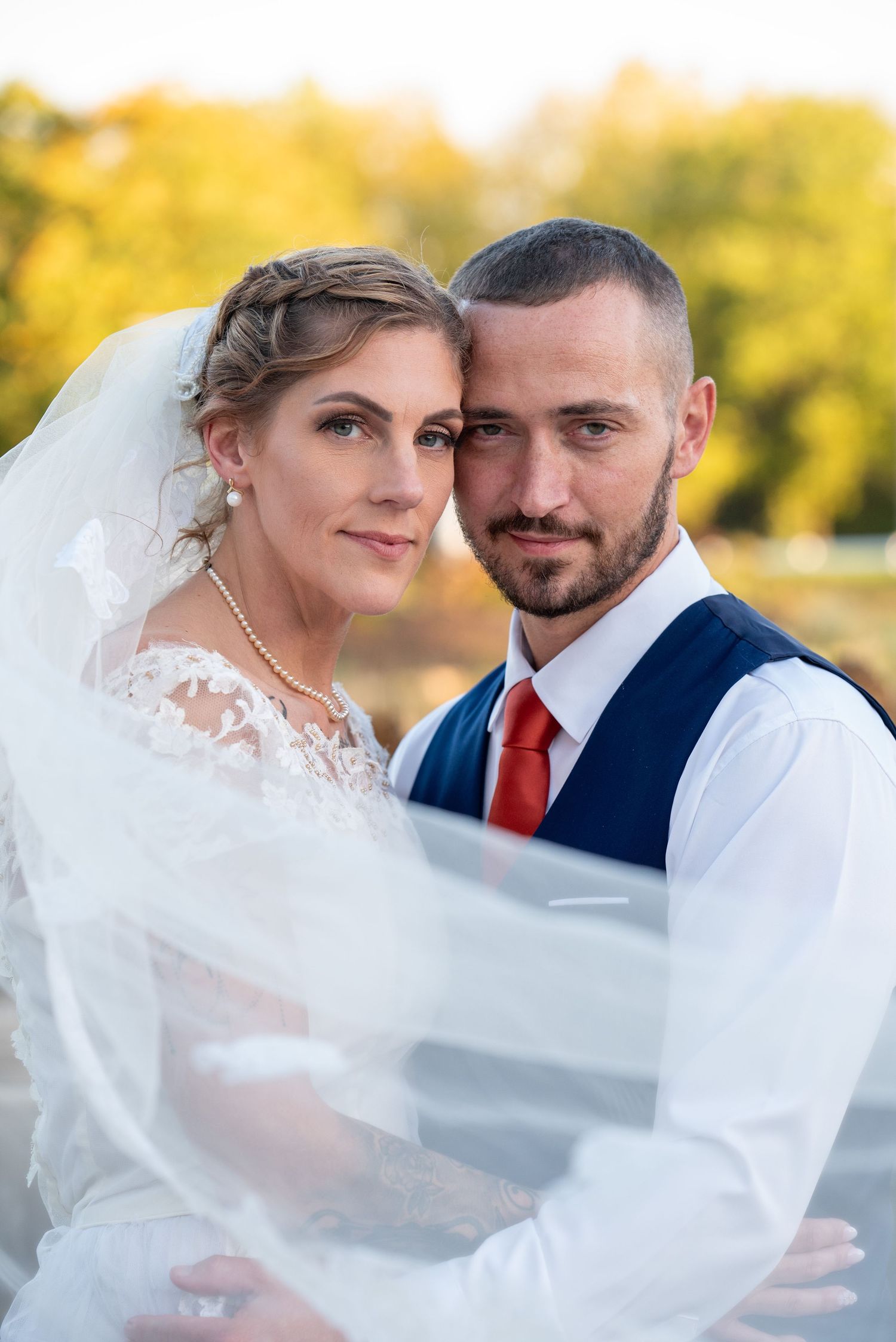 A romantic outdoor wedding portrait with a flowing veil captured in warm autumn sunlight.