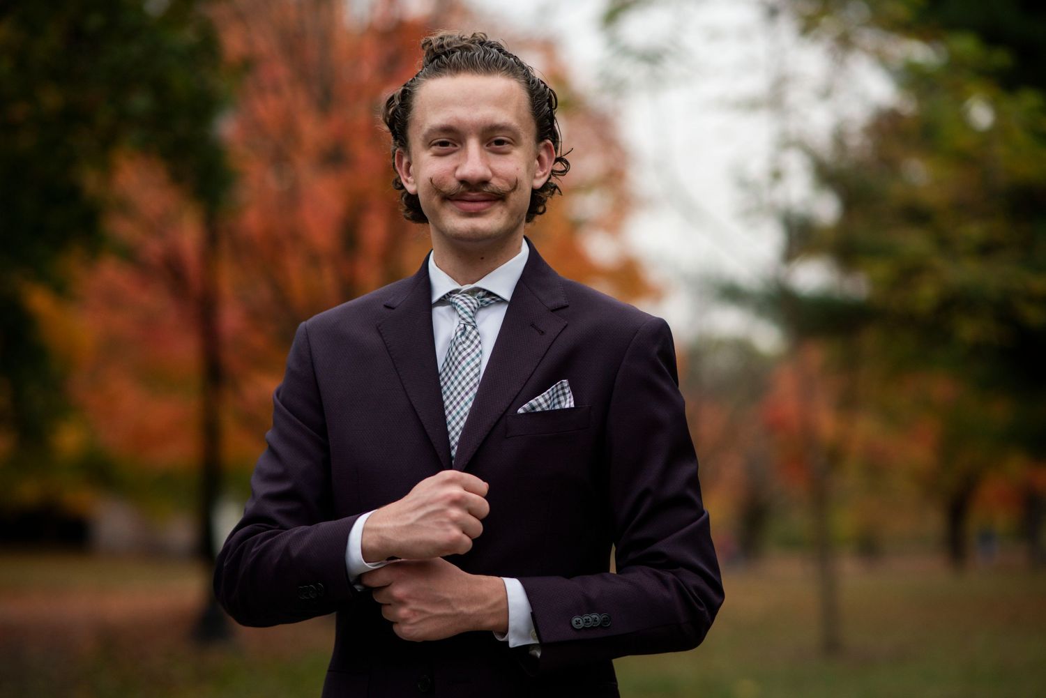 Professional portrait of man in dark suit with fall foliage background.