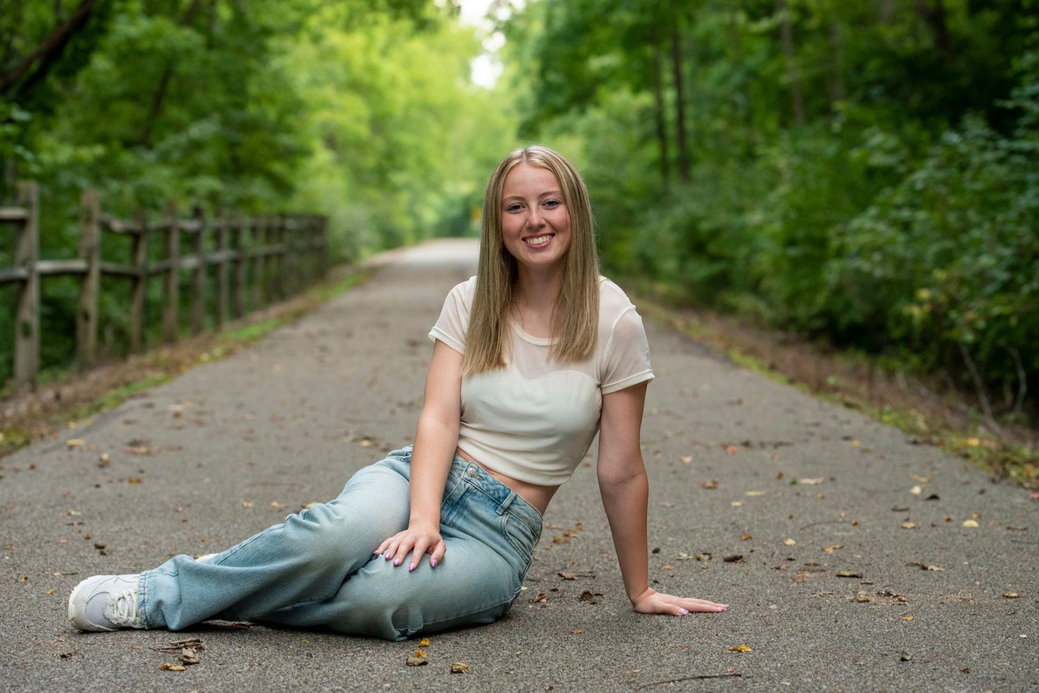Casual portrait of someone sitting on a tree-lined path in summer.