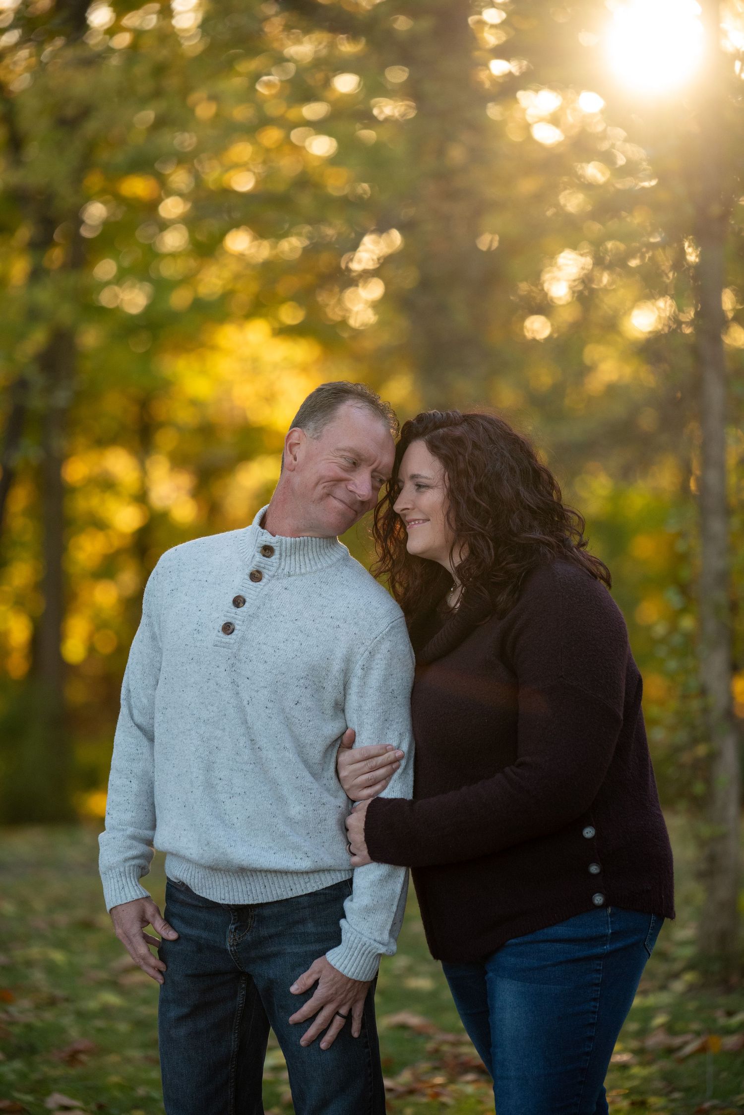 Intimate couple portrait in autumn forest with golden sunlight filtering through trees.