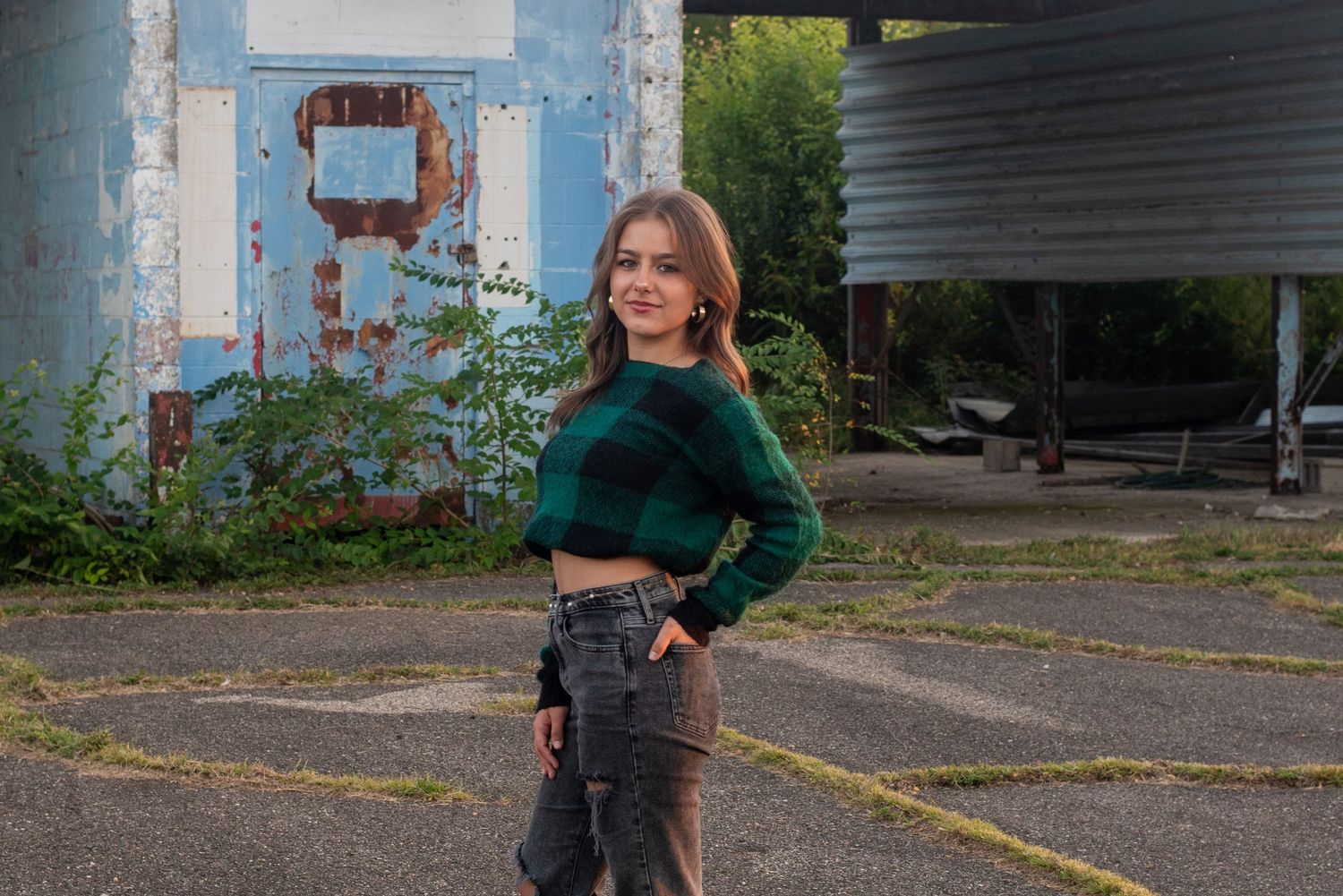 Fashion portrait against industrial backdrop wearing green crop top and dark pants.