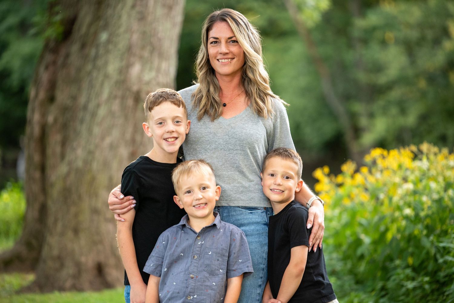 A family portrait taken outdoors with yellow flowers and greenery in the background.