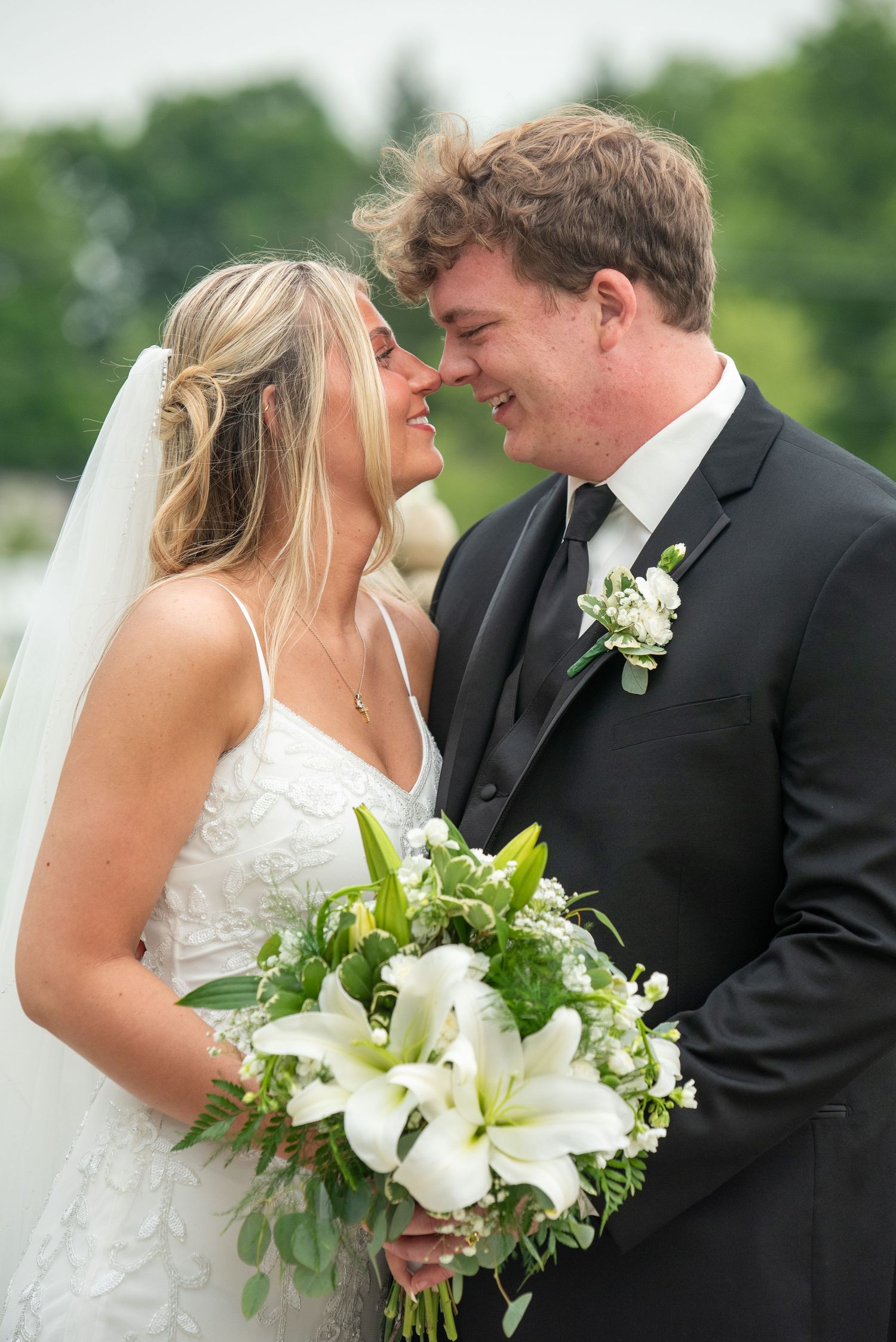 Elegant wedding couple embracing outdoors with a white lily bouquet.