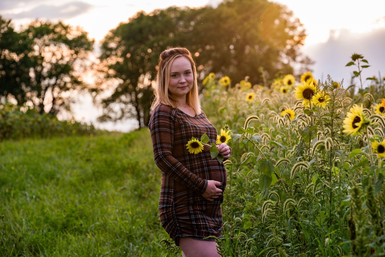 Woman in plaid poses in sunflower field during golden hour portrait session.