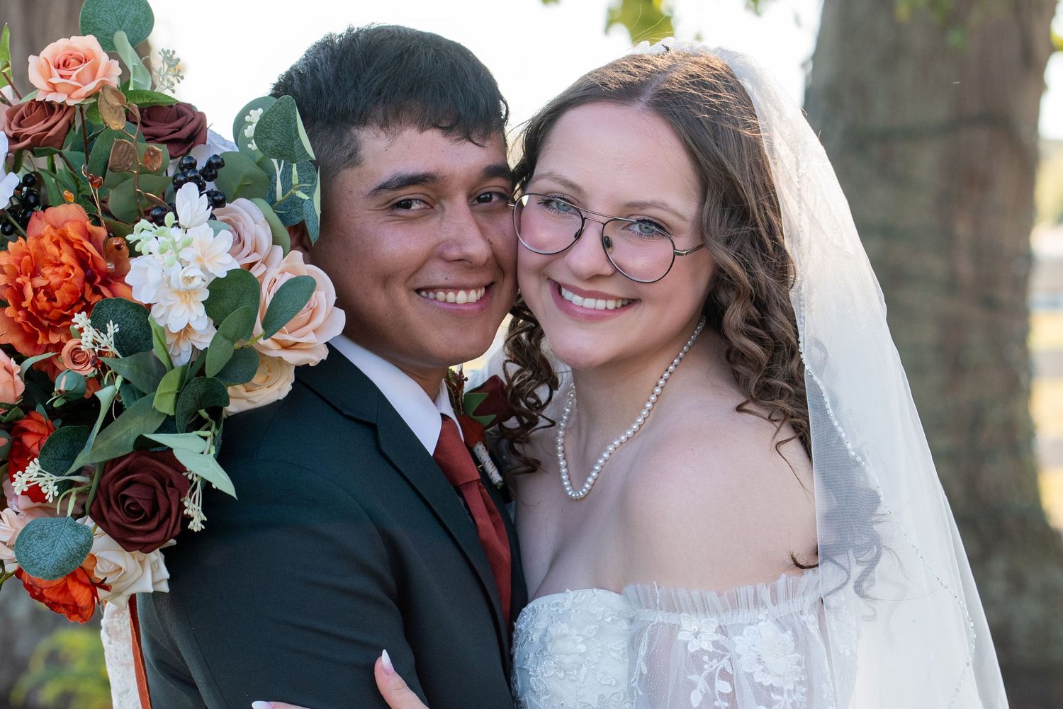 Wedding couple sharing intimate moments with autumn-colored floral bouquet.