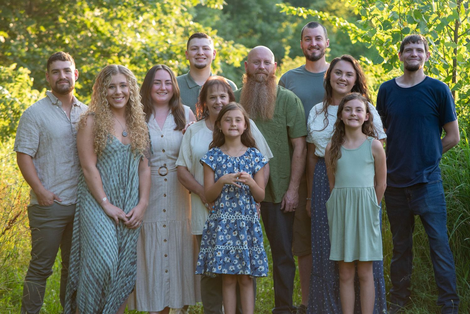 Large family group portrait taken outdoors during golden hour with trees in background.