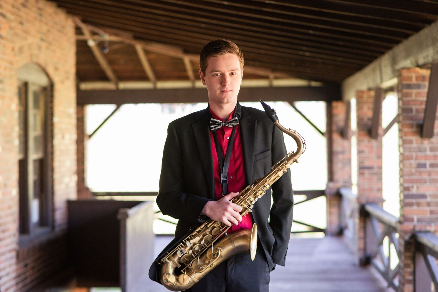 Professional musician in dark suit holding saxophone in covered outdoor walkway.