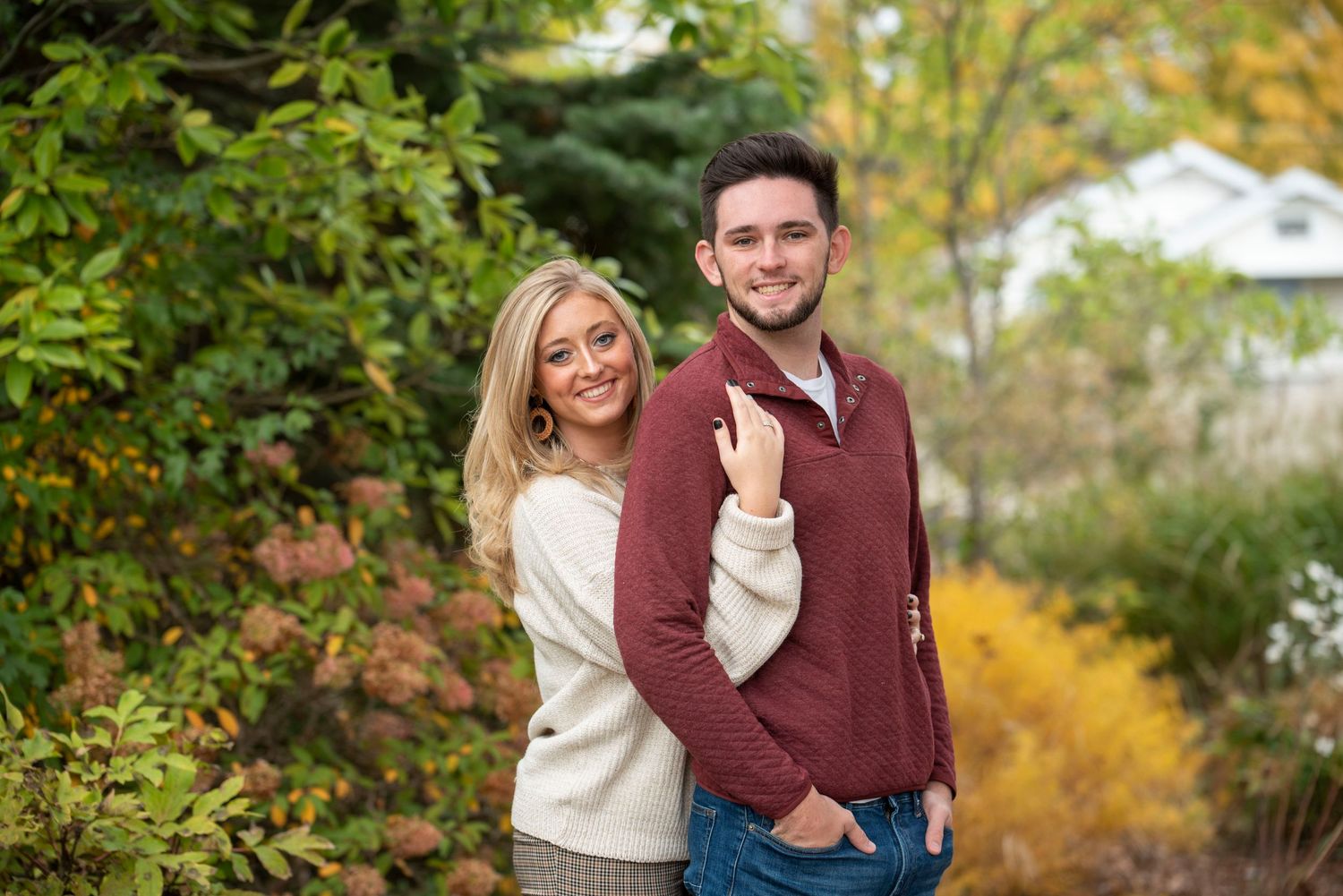 A playful autumn engagement photo with colorful fall foliage in the background.