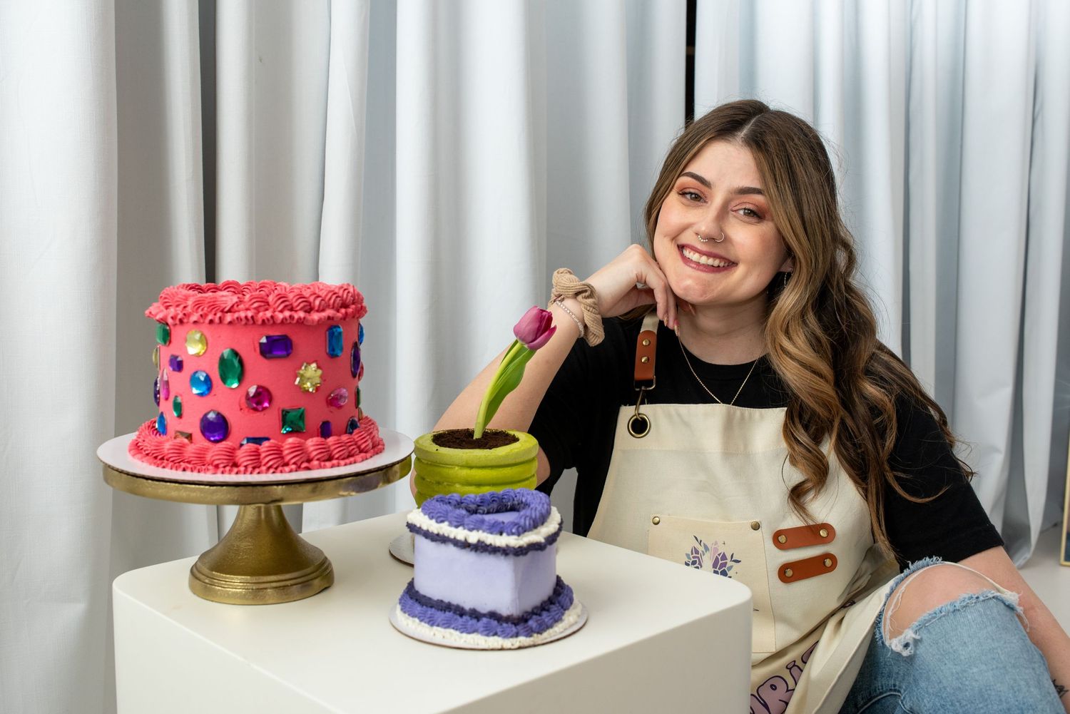 A collage of colorful cakes being decorated with frosting and berries on cake stands against a white curtain background.