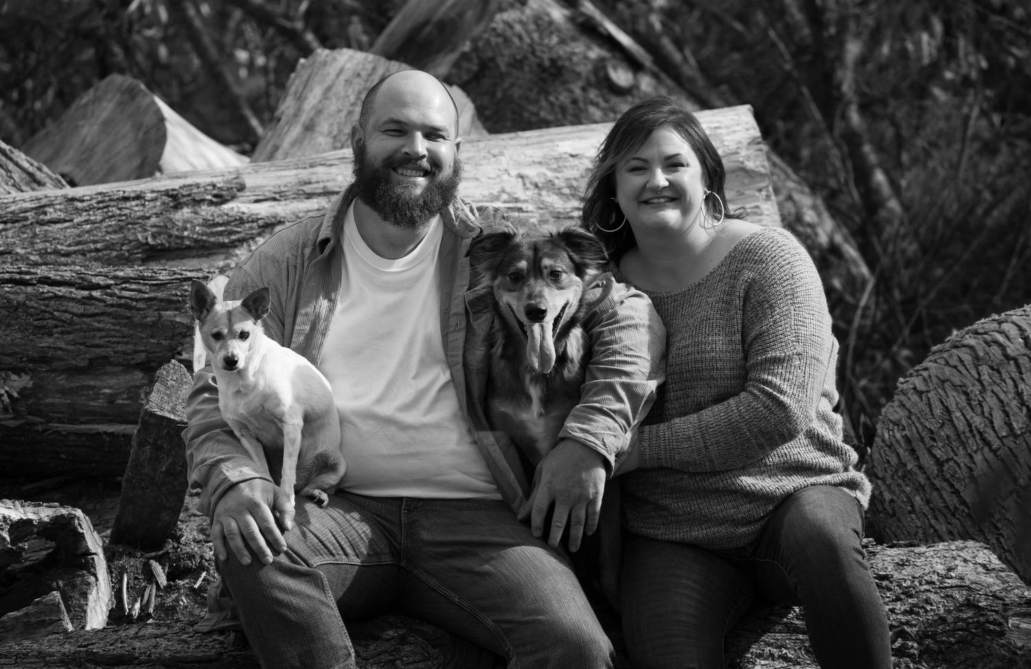 A couple sits outdoors with their two dogs during a photo session in autumn.