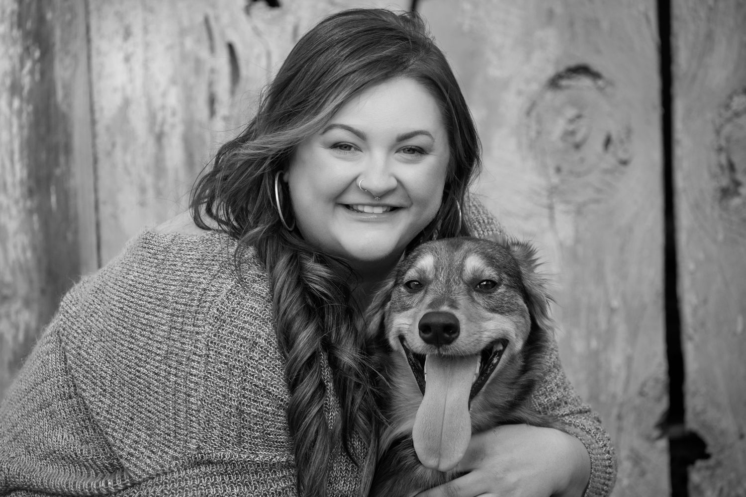 Woman in gray sweater embraces brown dog against weathered blue wall.