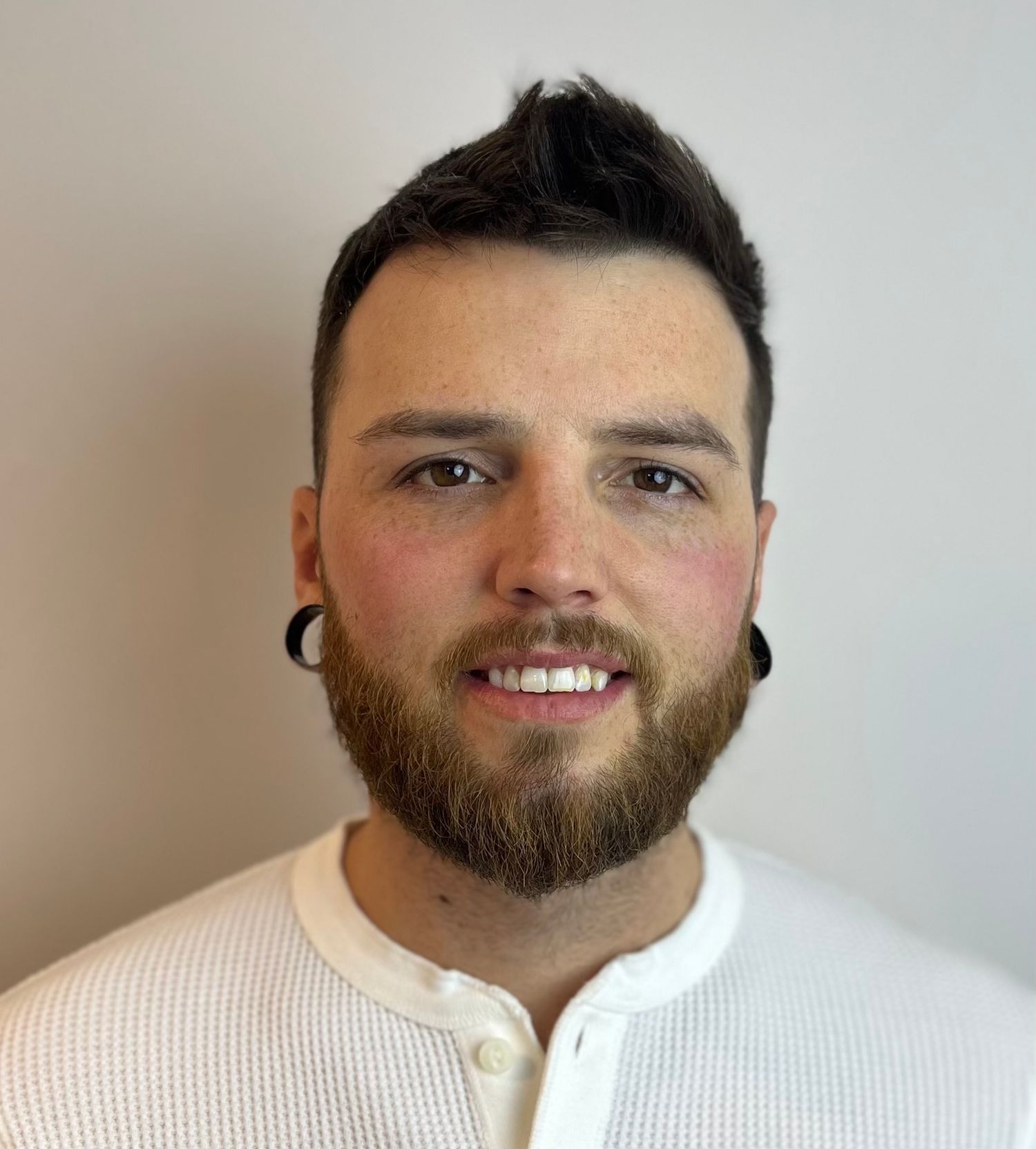 Smiling person with dark beard wearing white collared shirt in progression of headshot poses against light background.