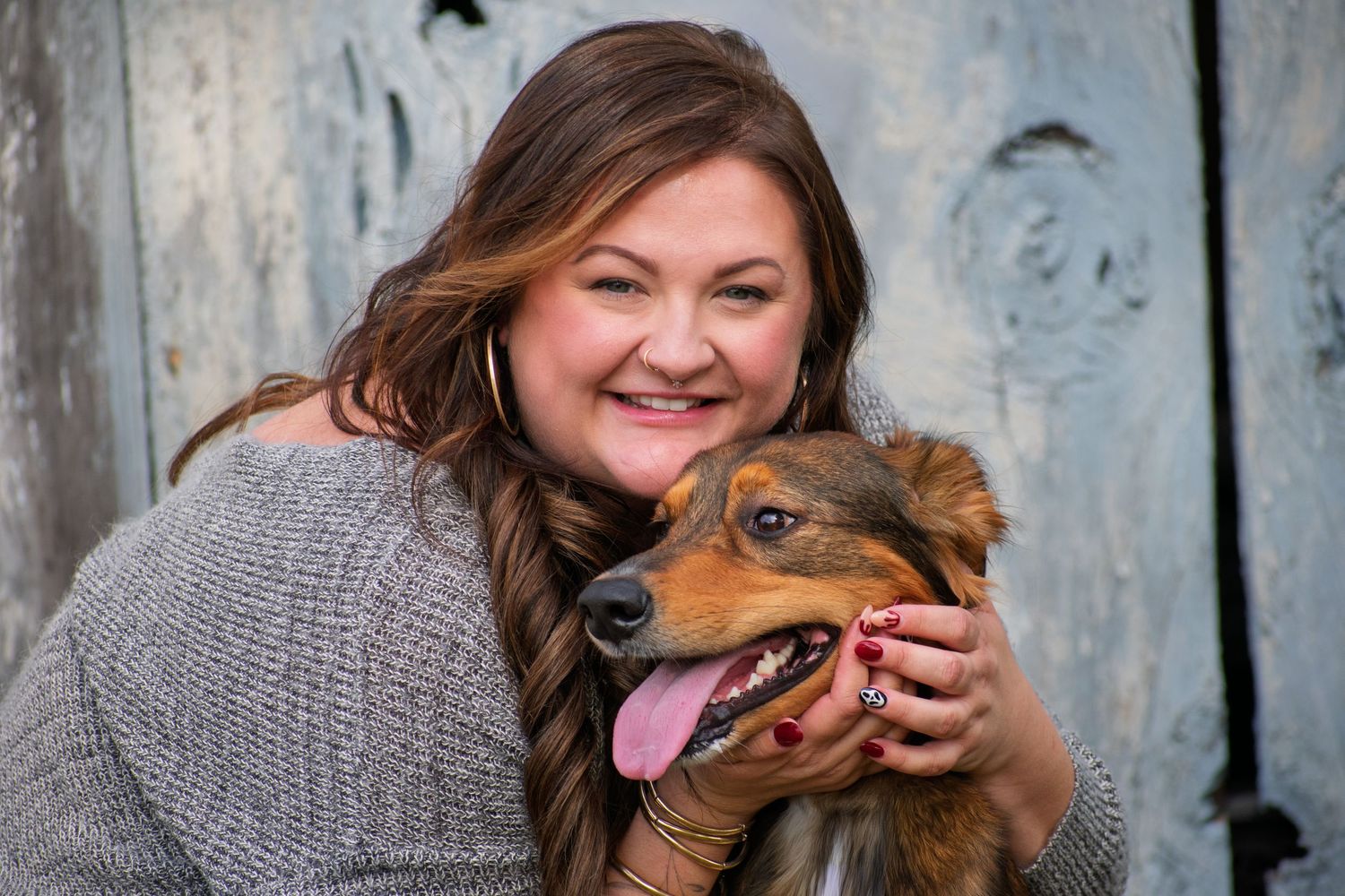 Woman in gray sweater shares joyful moment with brown dog.