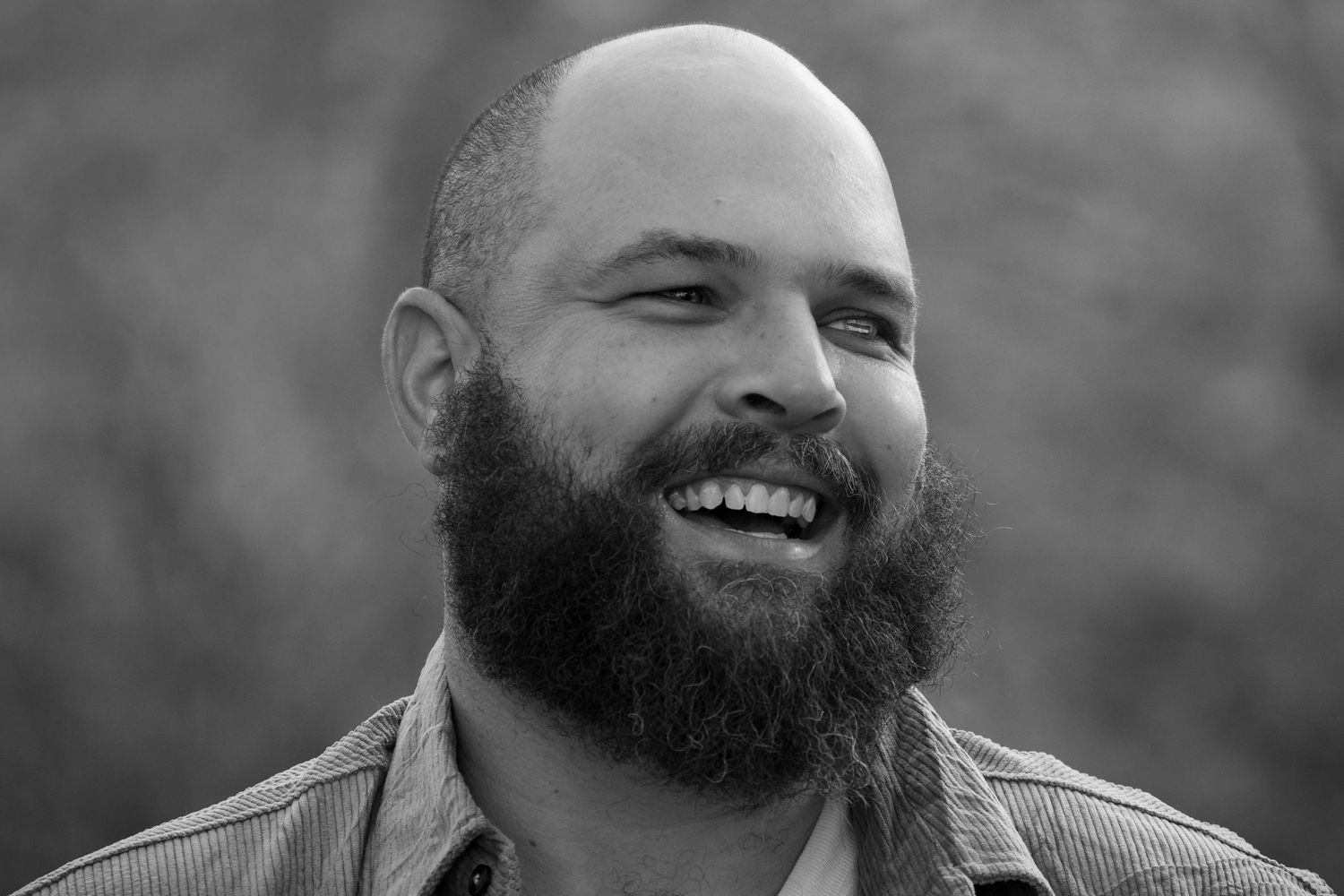 Black and white portrait of bearded man laughing against blurred background.