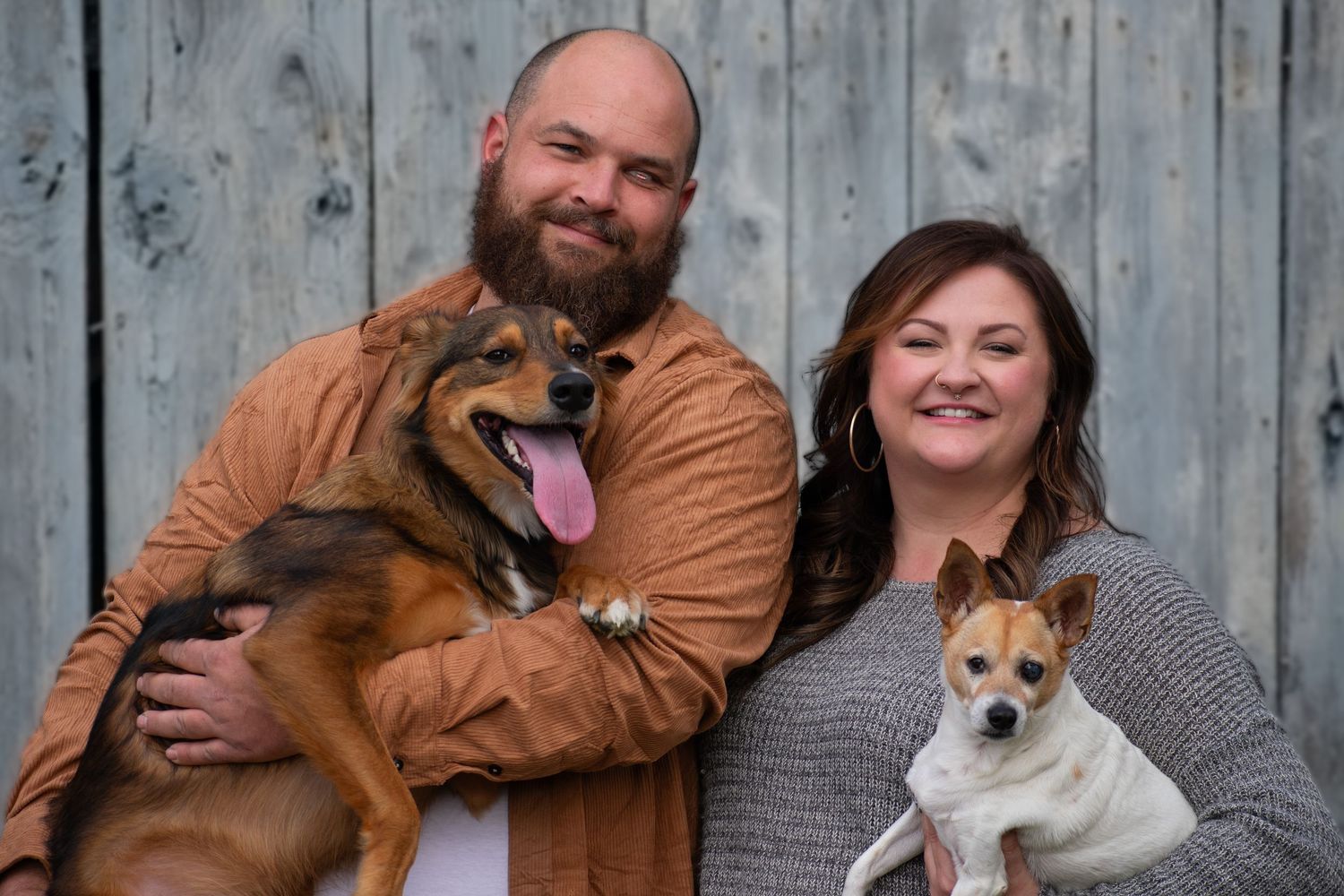 Family portrait with two dogs against rustic wooden background.