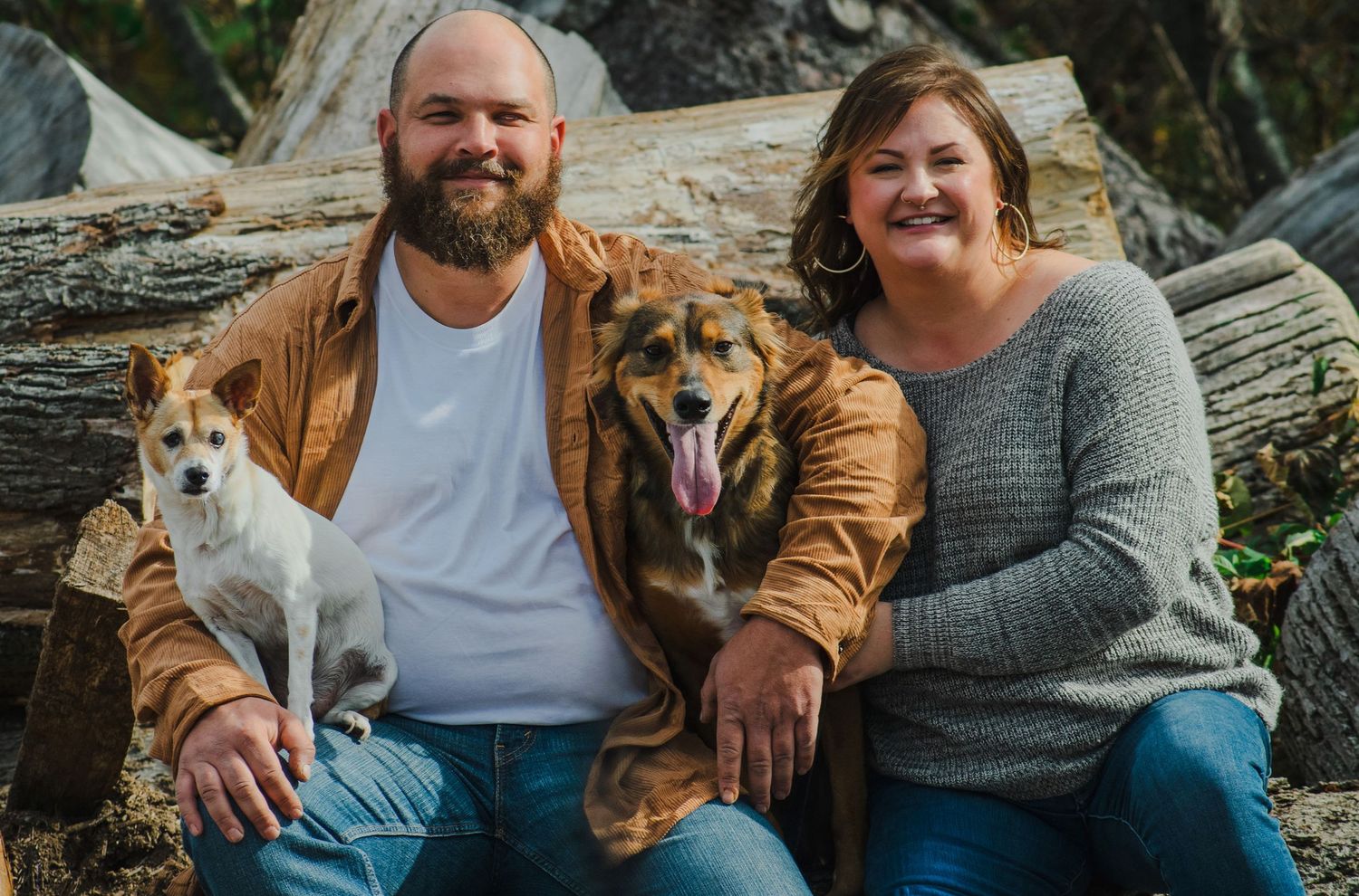 A couple sits on a log with their three happy dogs during an outdoor photo session.