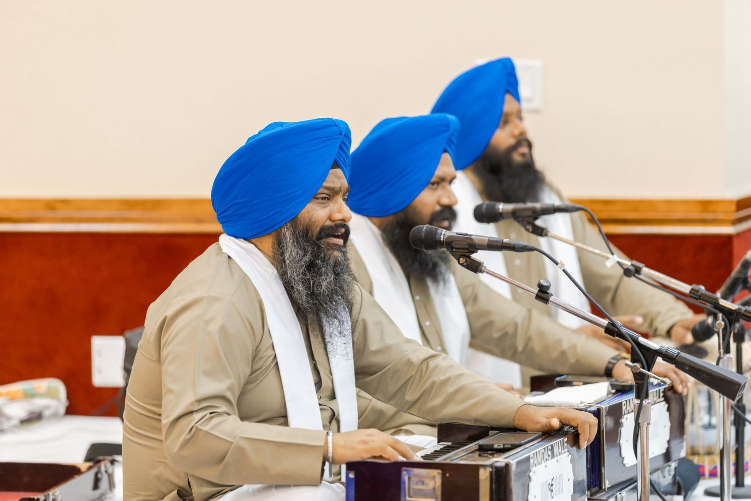 Musicians in traditional Sikh attire performing with instruments at a ceremonial event.