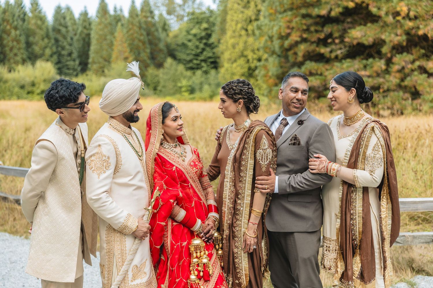 Wedding party standing together in formal attire outdoors with trees and meadow in background.