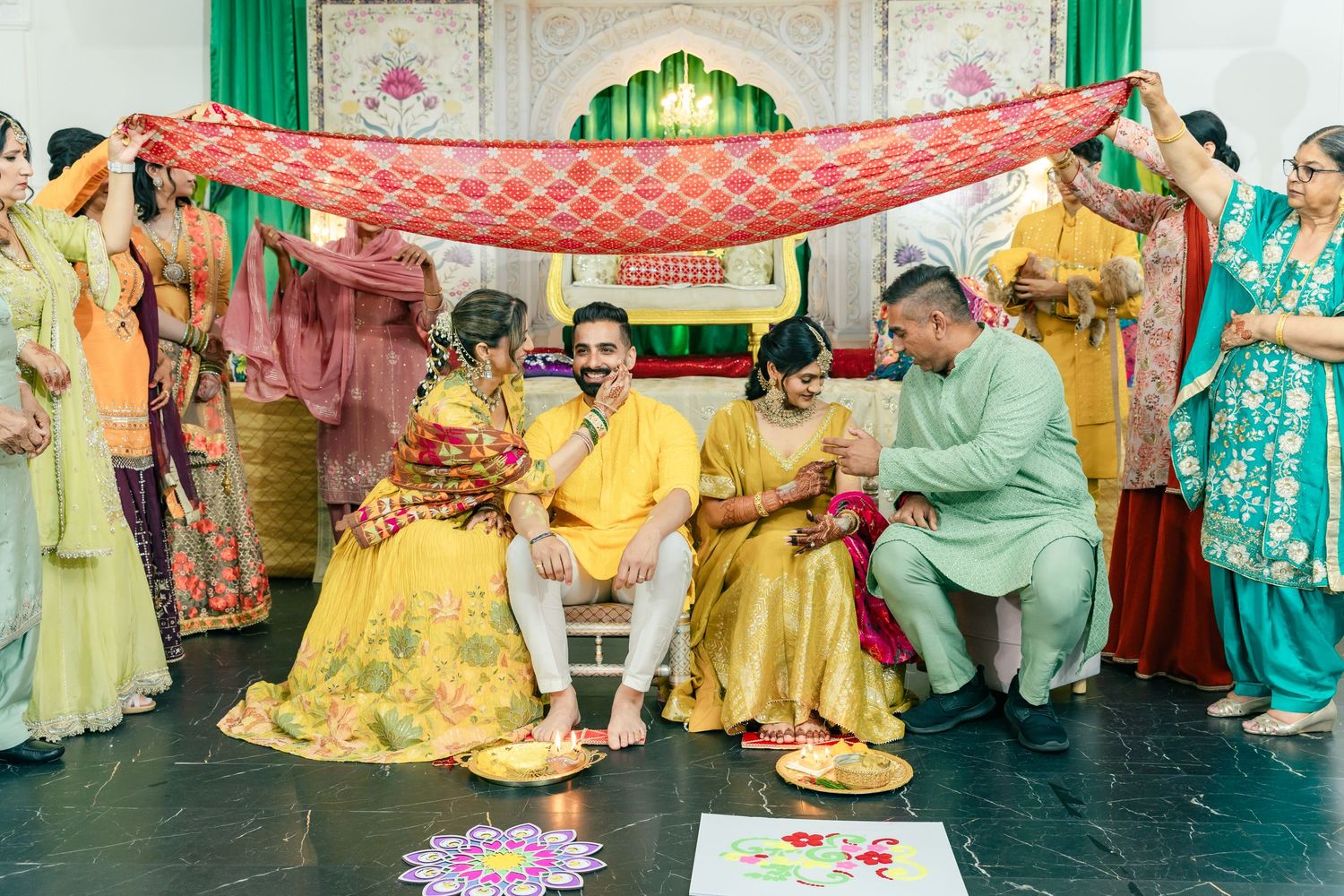 Traditional wedding celebration with guests in colorful attire gathered under decorative drapes and archways.