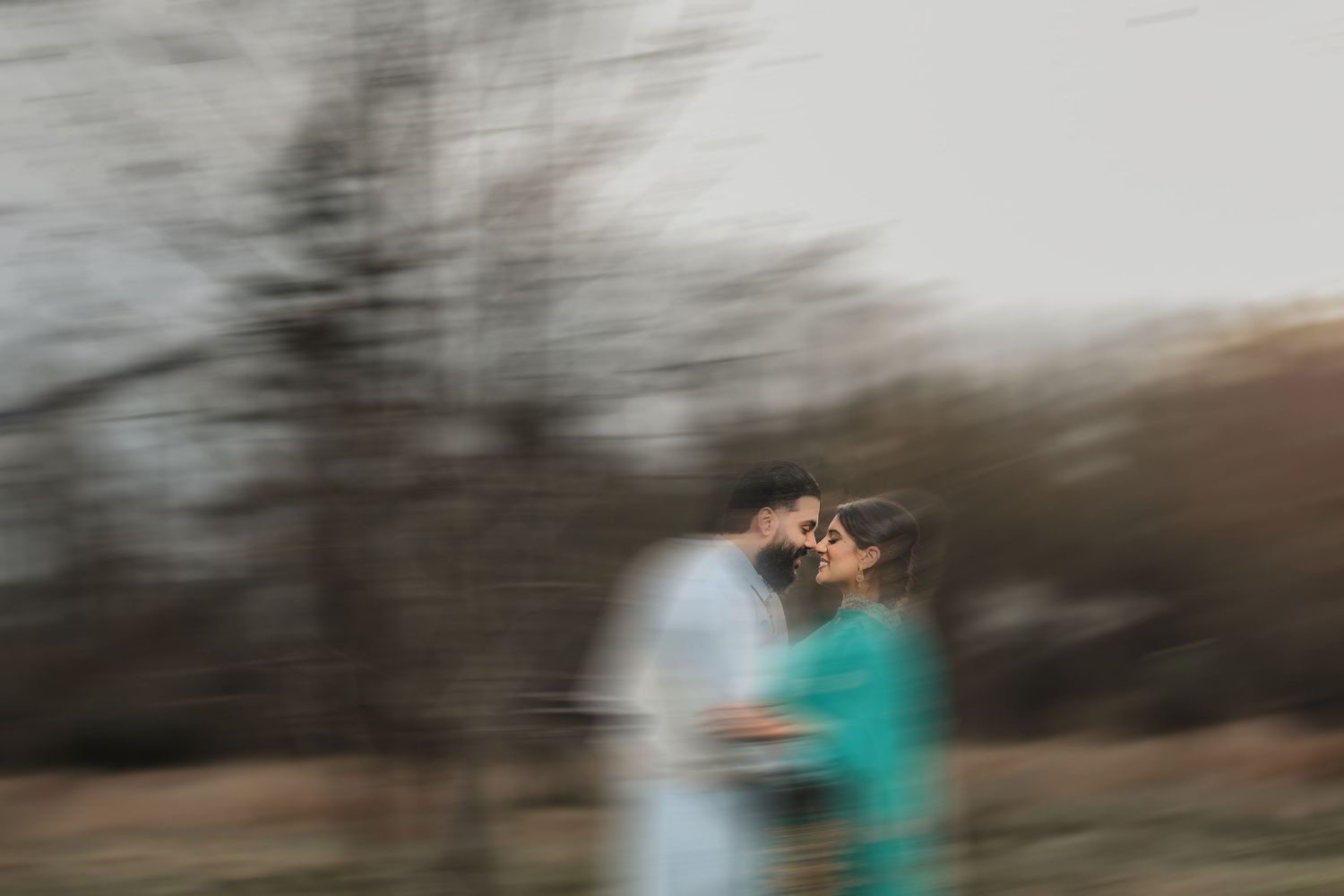 Couple posing together under bare winter trees during a moody outdoor photoshoot.