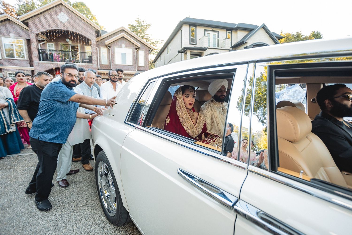 Wedding guests bid farewell to couple departing in classic white luxury car.