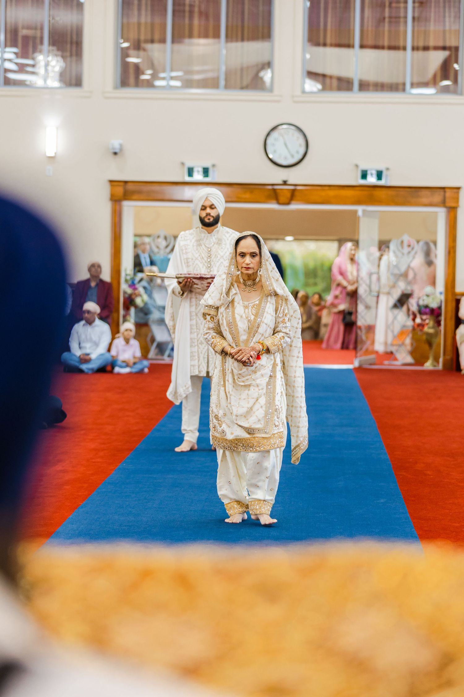 Wedding ceremony procession on blue carpet in a bright indoor venue.