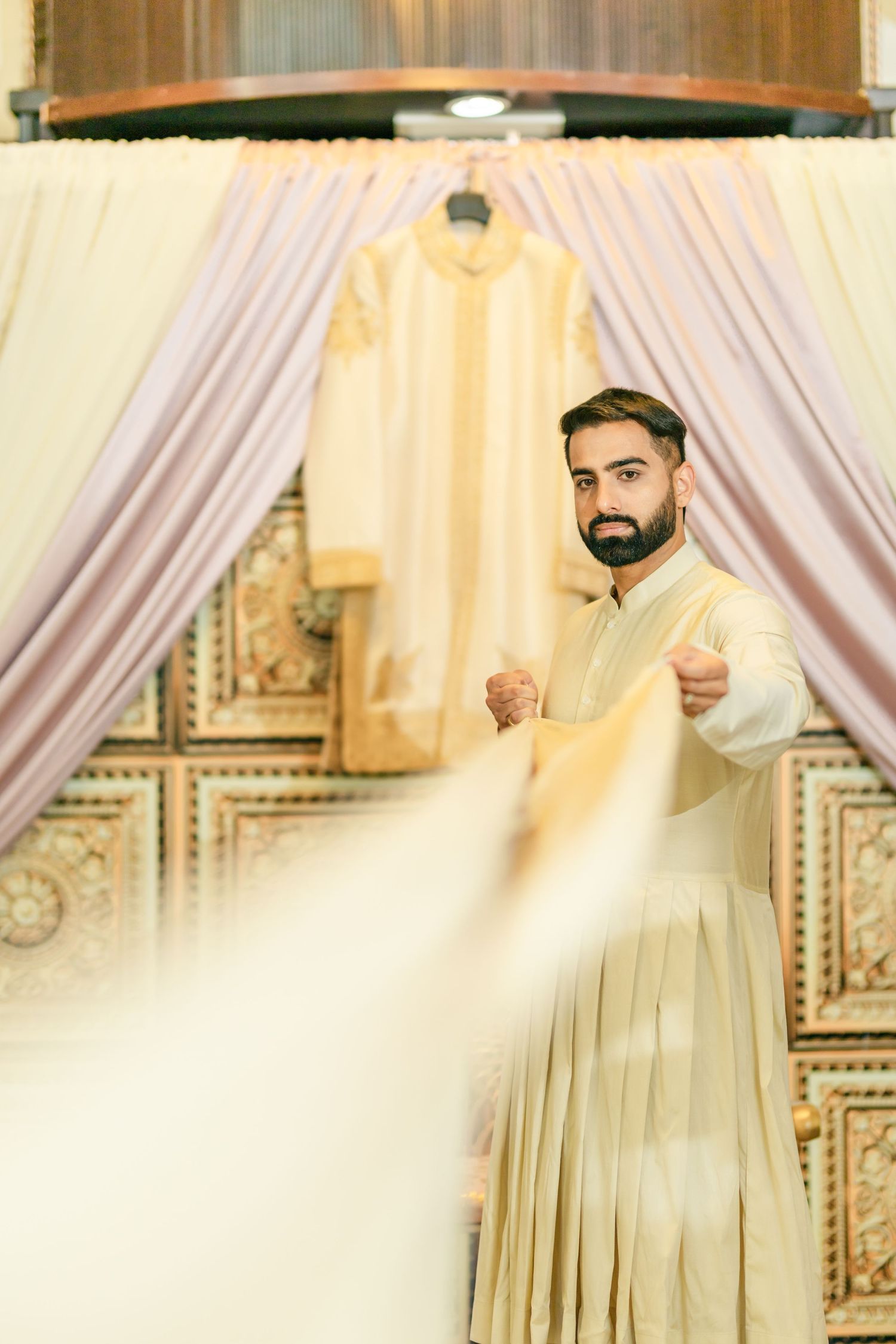 Elegant wedding ceremony setup with white drapes and traditional Indian decor in a bright indoor venue.