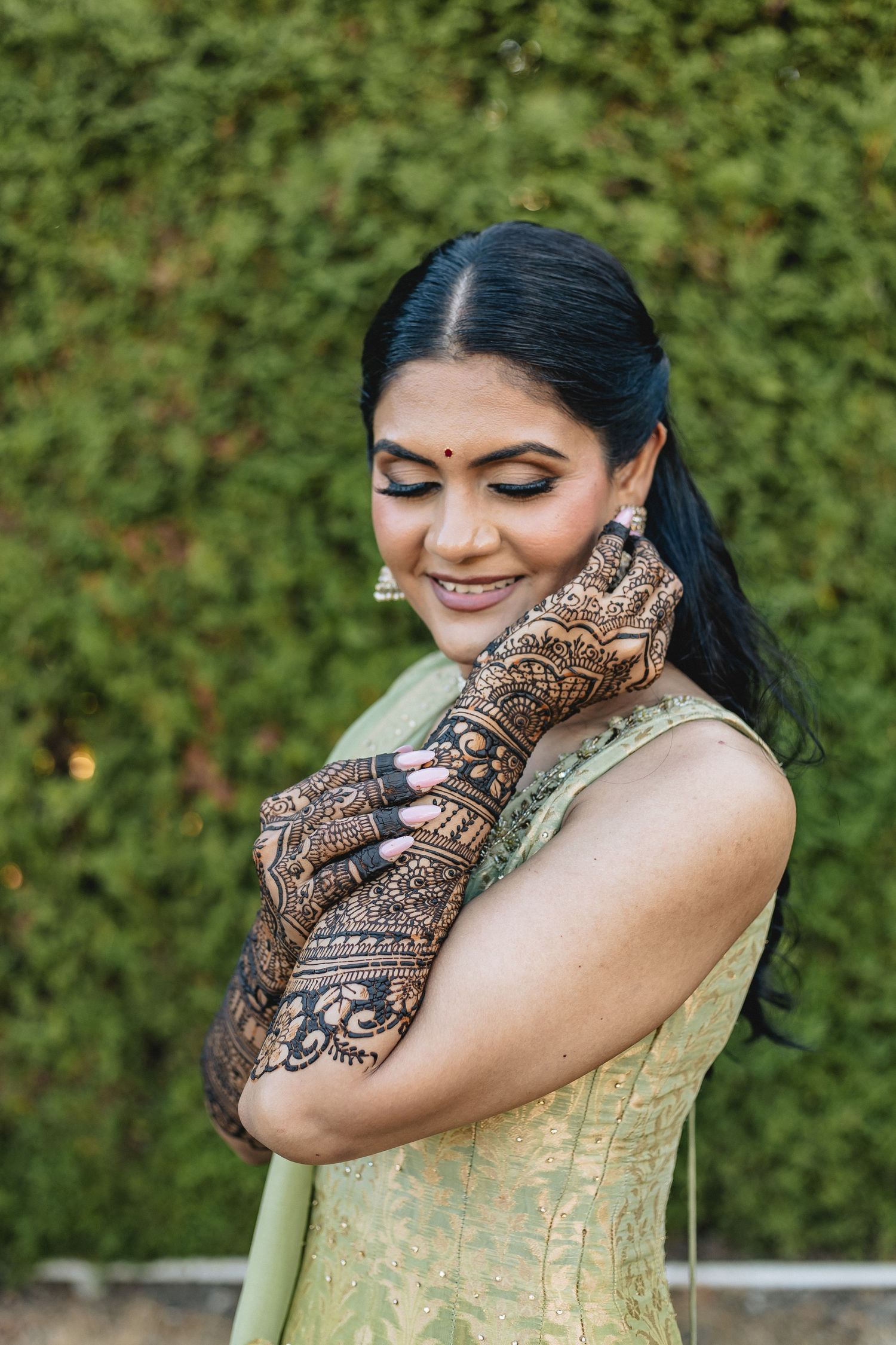 Intricate henna design displayed on hands with a green hedge background.