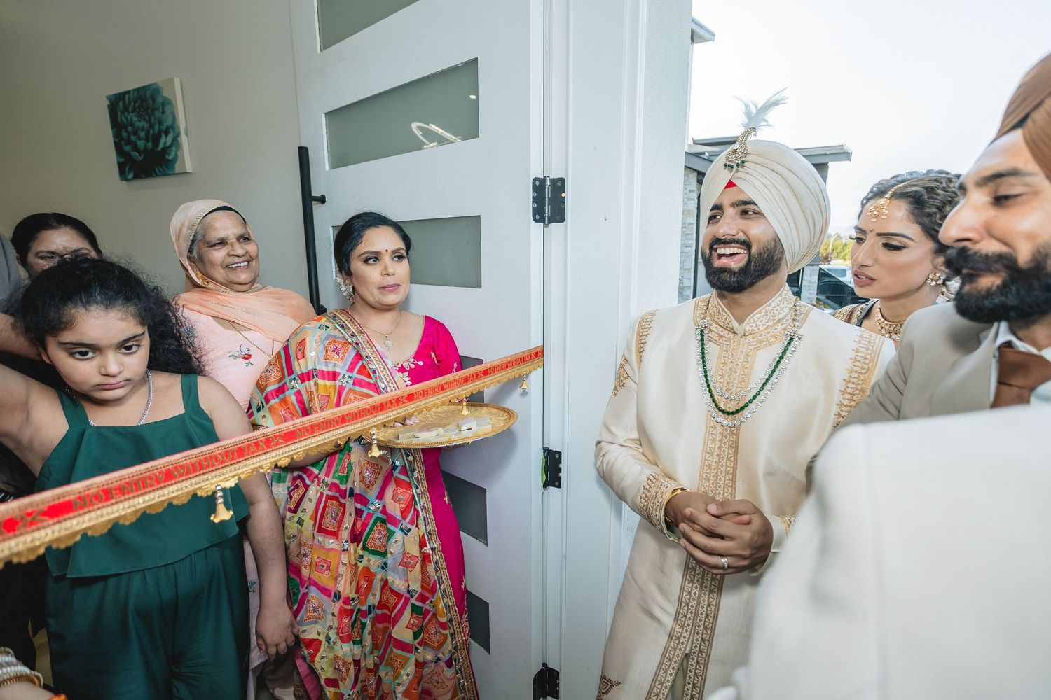 Wedding party members in traditional Indian attire gathered in a bright indoor hallway.