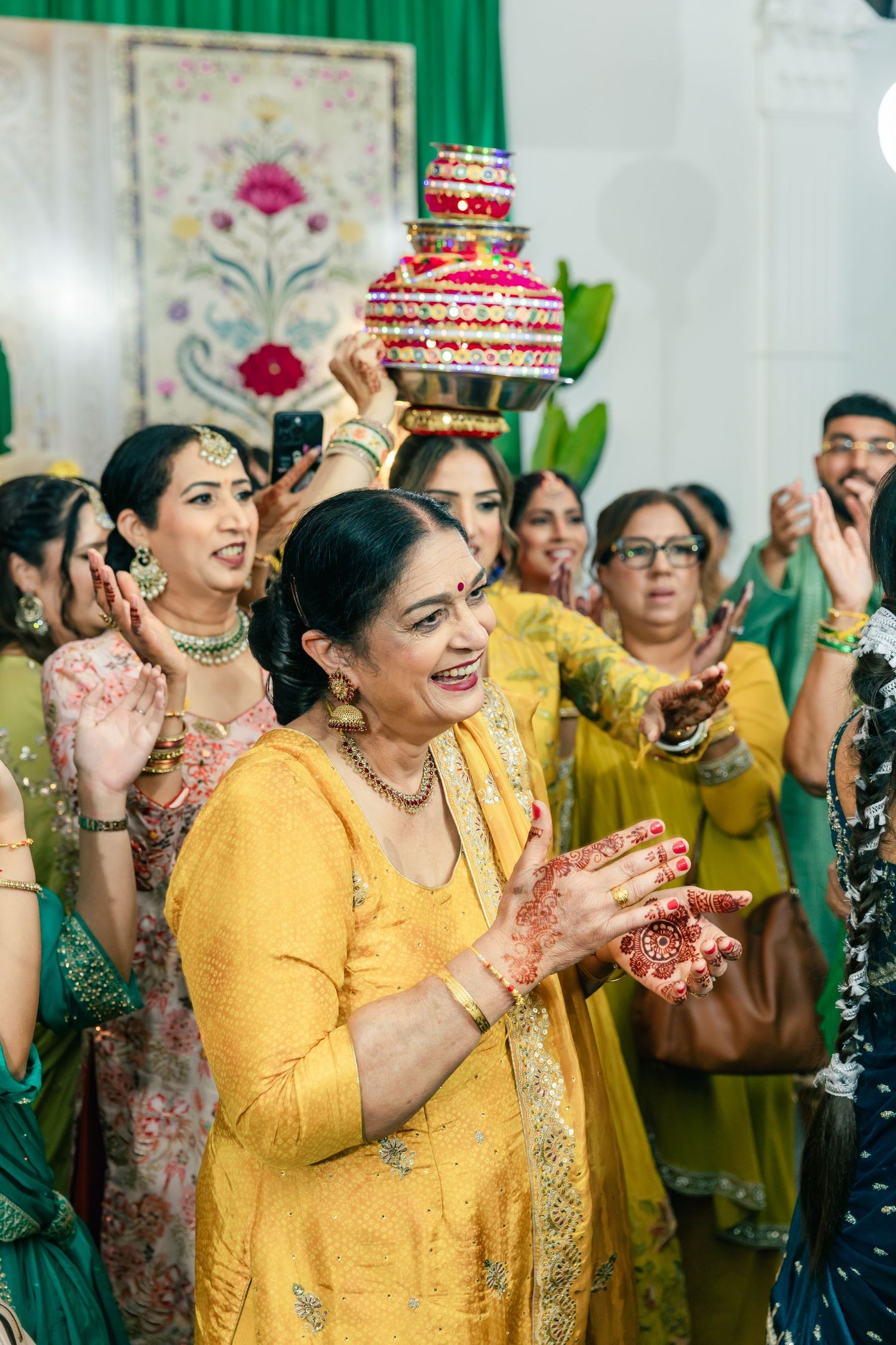 Wedding guests in yellow attire celebrate with traditional red decorative pots balanced on their heads.