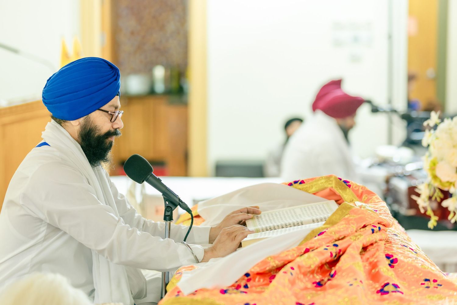 Sikh men in traditional dress and blue turbans work at sewing machines in a garment factory.