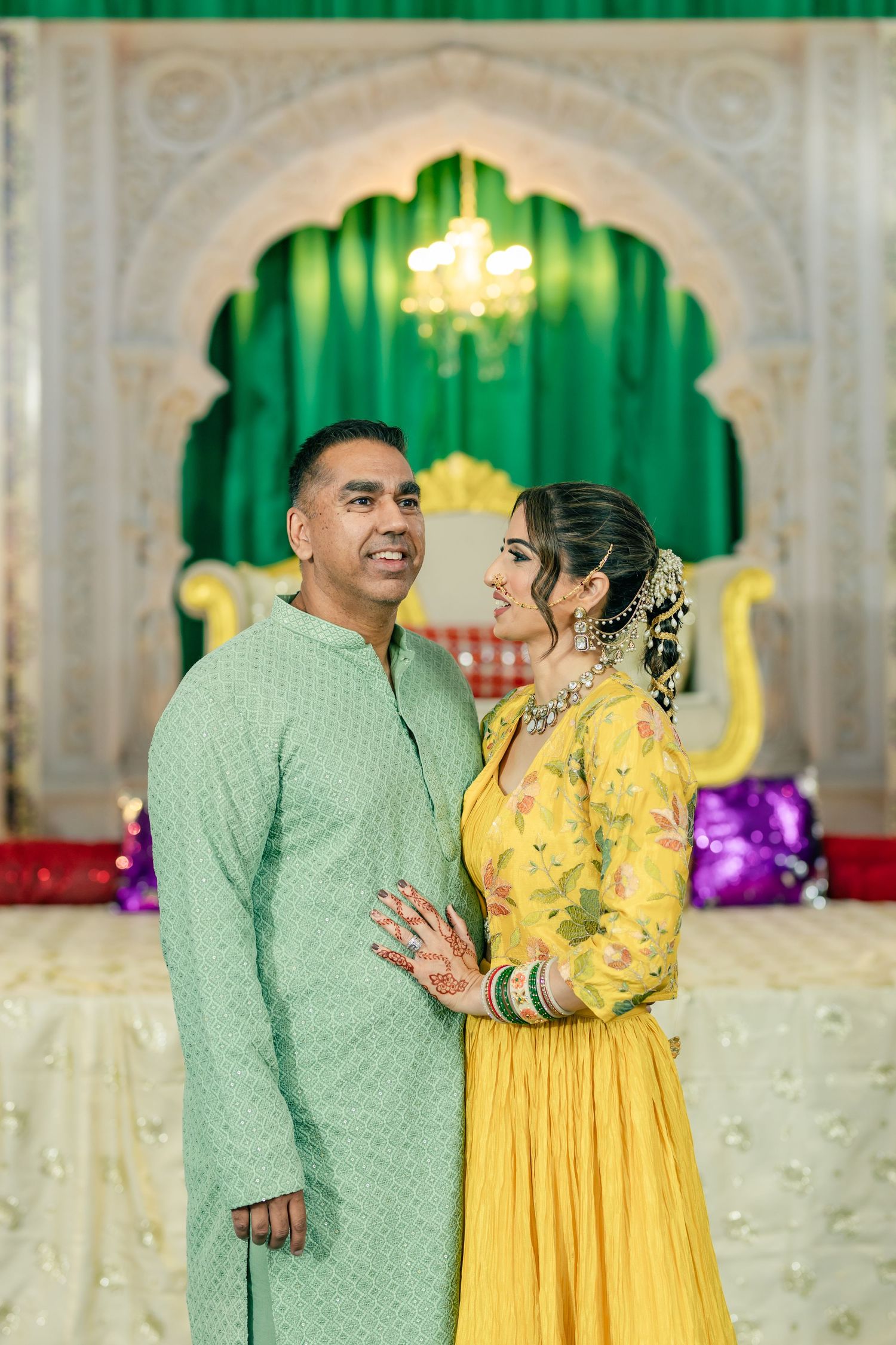 A couple in traditional Indian attire, wearing mint green and yellow outfits, share joyful moments during a celebration.