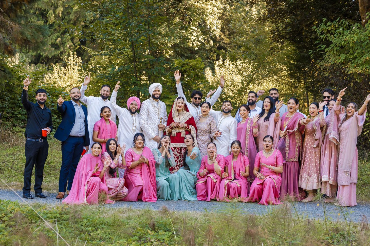 Wedding party in pink and pastel outfits poses together outdoors in natural setting.