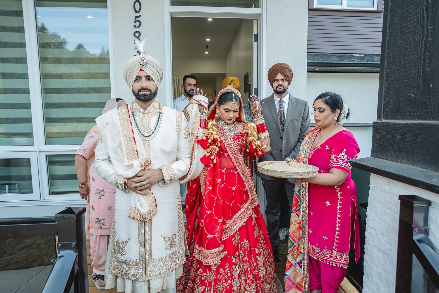 Wedding party members in traditional Indian attire gathered outside a white building entrance.
