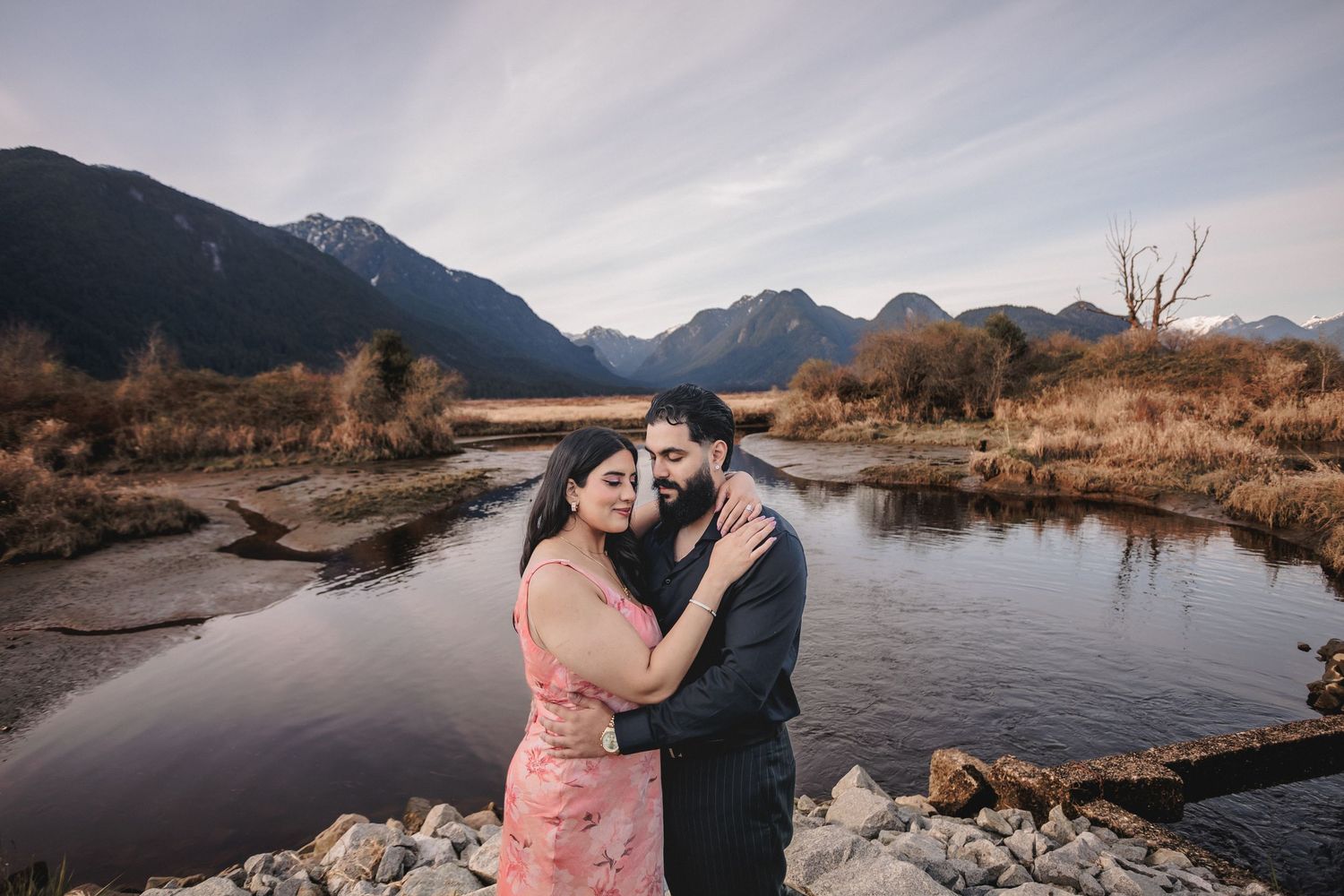 A romantic photoshoot by a mountain lake with dramatic cloudy skies in the background.