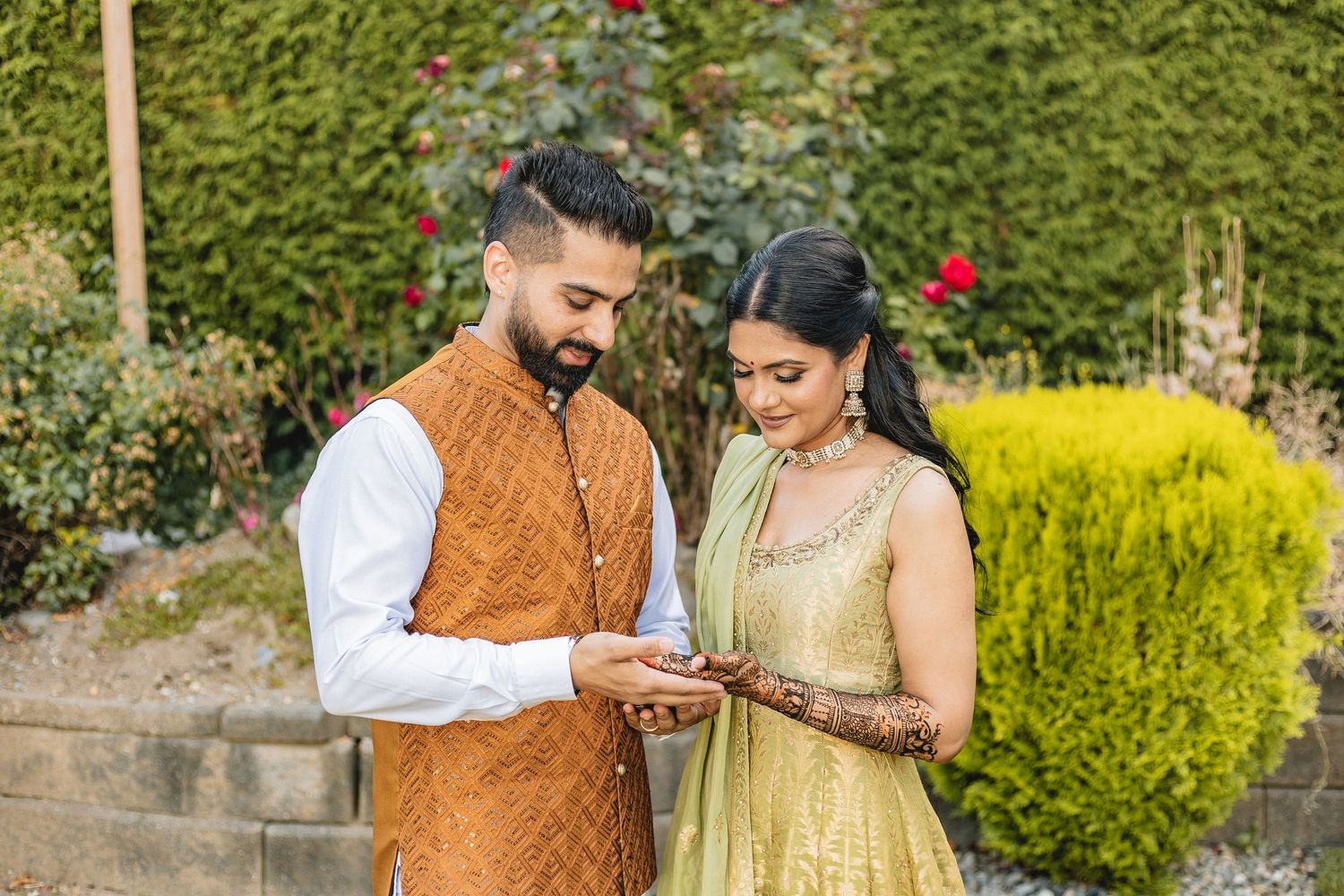 A couple in traditional Indian attire shares a romantic moment in a garden setting with yellow flowers.