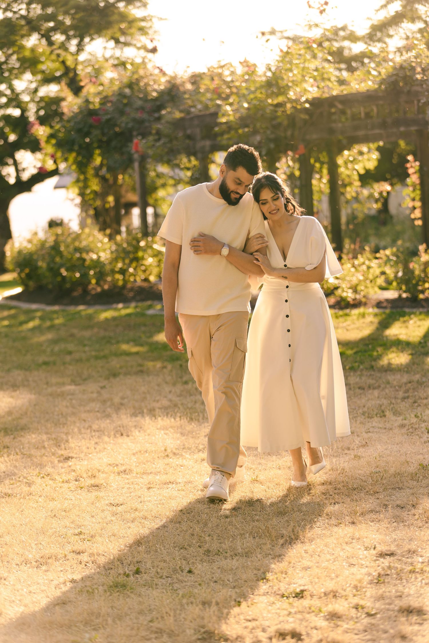 Two people in cream-colored clothing walk together on a grassy hill during sunset.