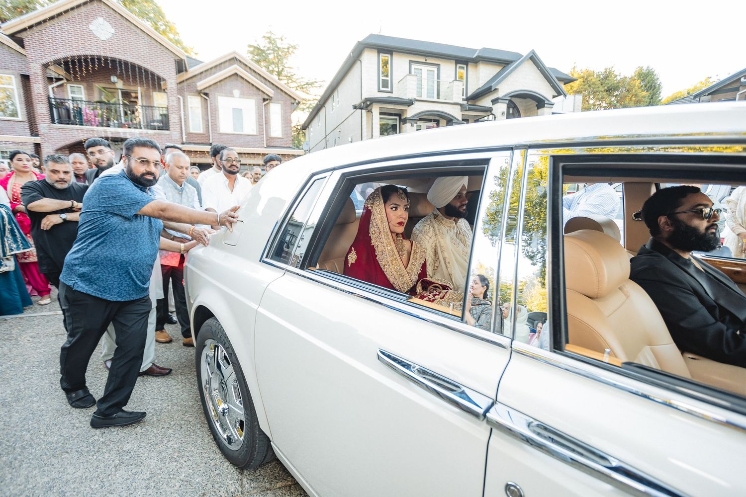 Classic white vintage car parked outside with wedding guests gathering around.