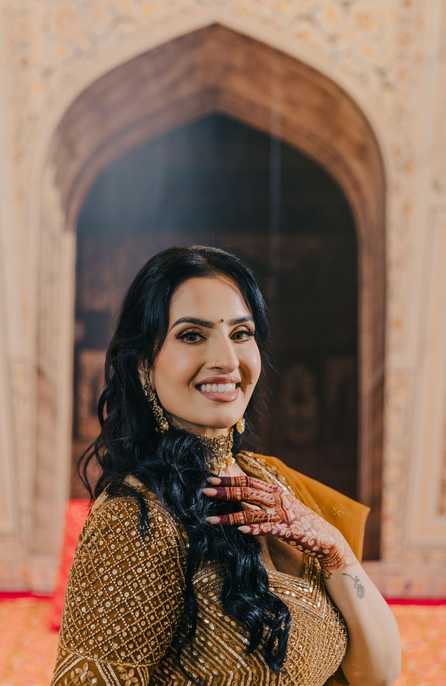 Woman in golden traditional attire poses elegantly in front of architectural arches.