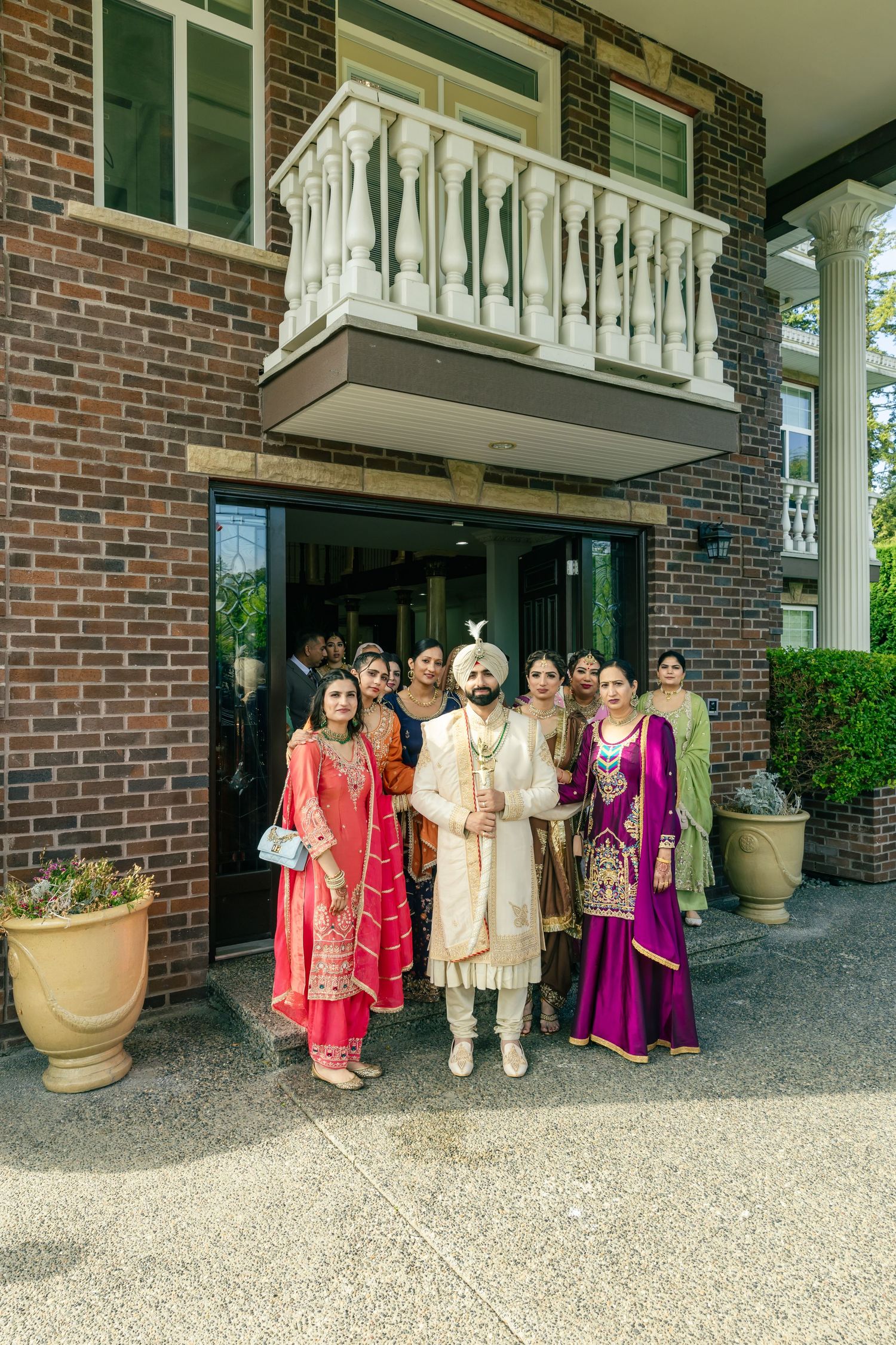 Wedding party gathered outside brick building entrance wearing traditional Indian attire.