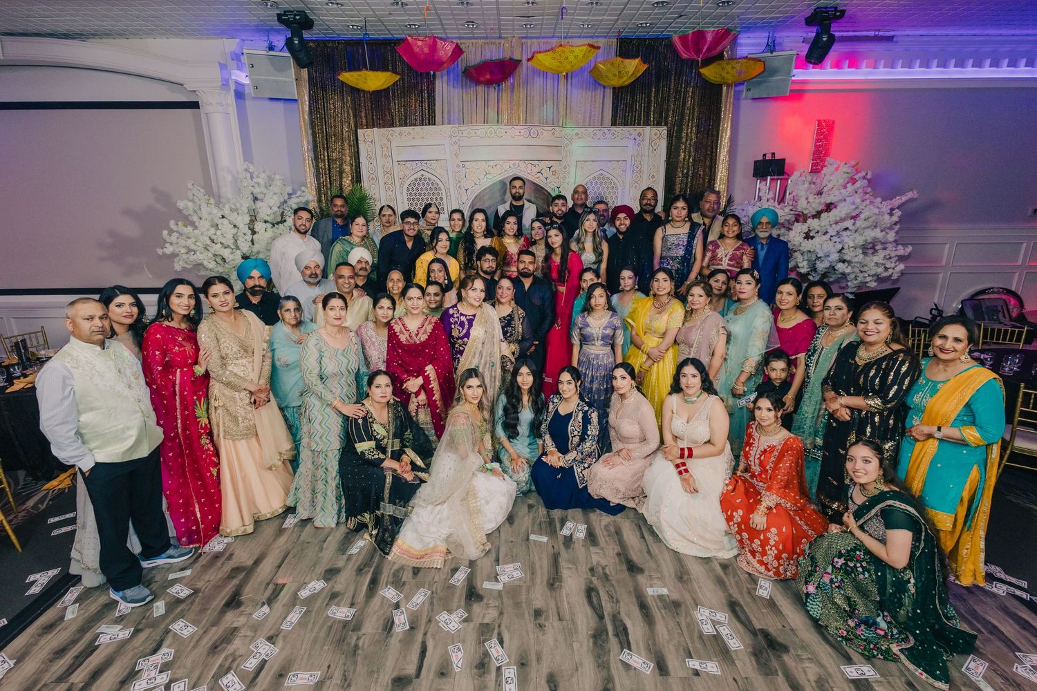 Large group photo of wedding guests posing together in formal attire against a decorated backdrop.