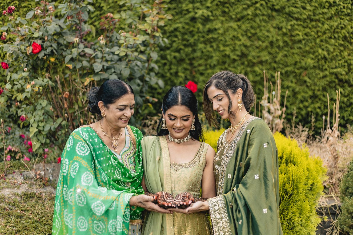 Guests in colorful traditional attire gather outdoors near blooming red flowers and greenery during a celebration.