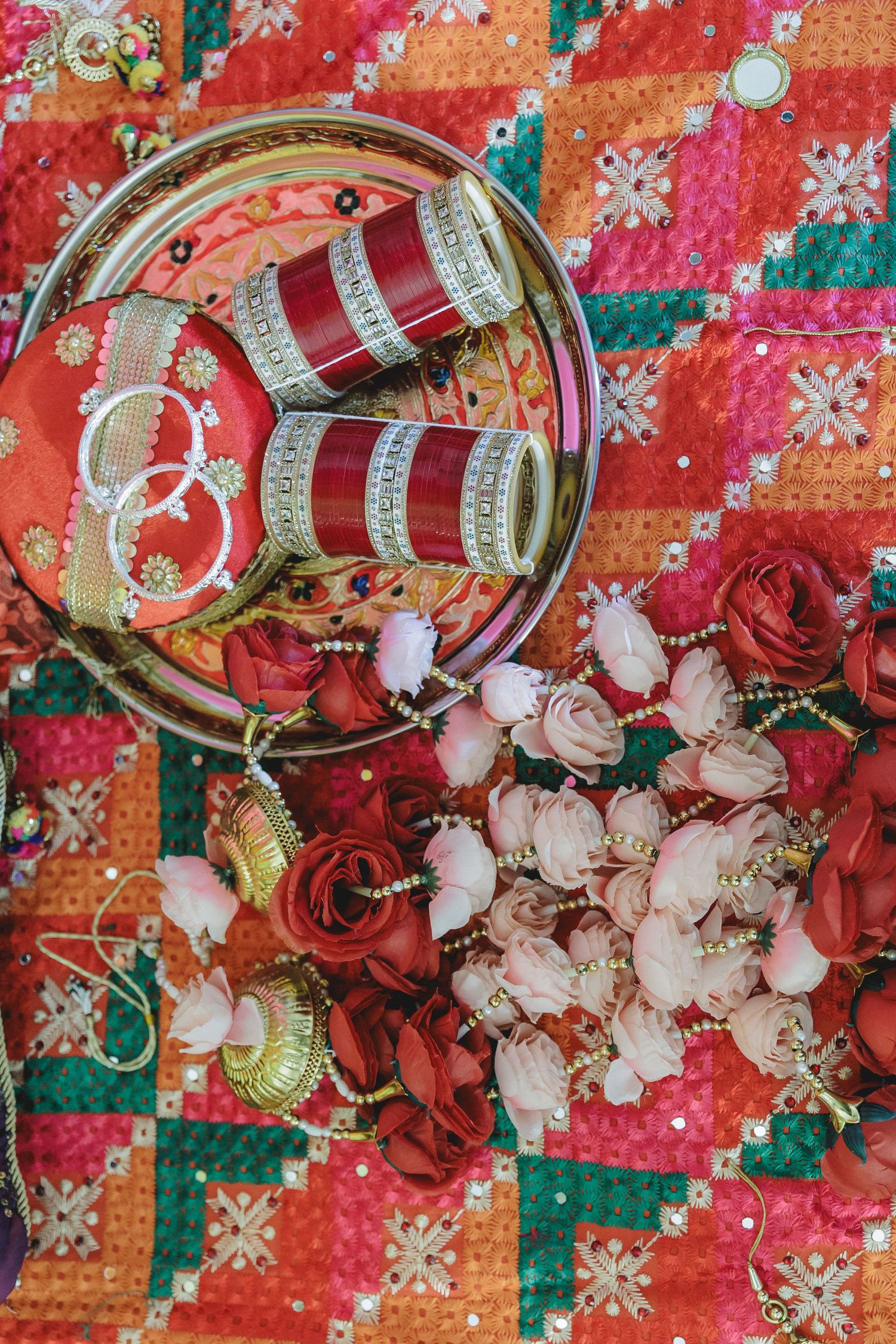 Traditional Indian wedding bangles and roses arranged on colorful patterned fabric.