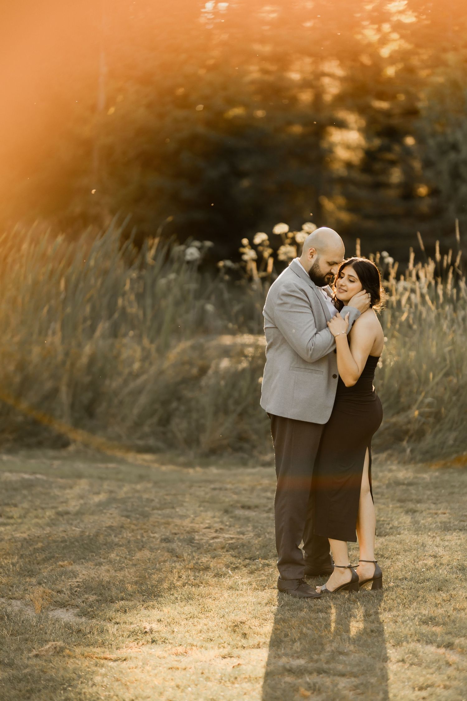 A romantic sunset photoshoot featuring a couple embracing in a golden field during magic hour.